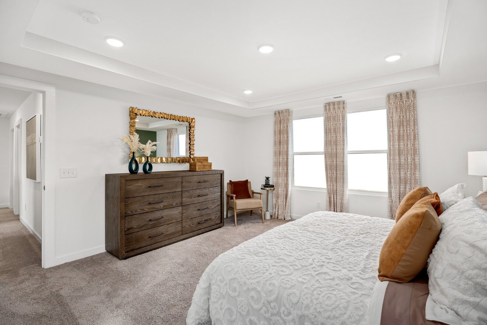 Elegant master bedroom with king bed, gold mirror, wood dresser, and large windows in Davidson Homes The Gordon C, White House, TN
