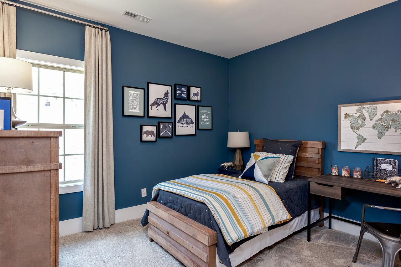 Navy blue boy's bedroom in The Rockford by Davidson Homes: wooden twin bed with striped duvet, desk, world map, dog posters, lamp