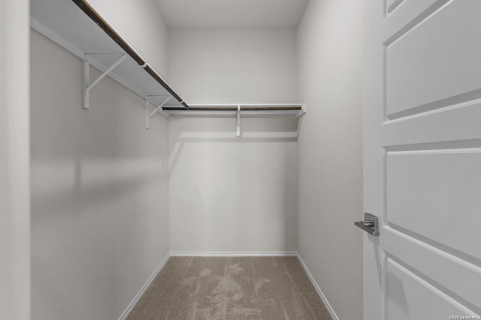 Walk-in closet with carpet flooring and shelving in The San Marcos F floor plan by Davidson Homes in San Antonio, Texas.