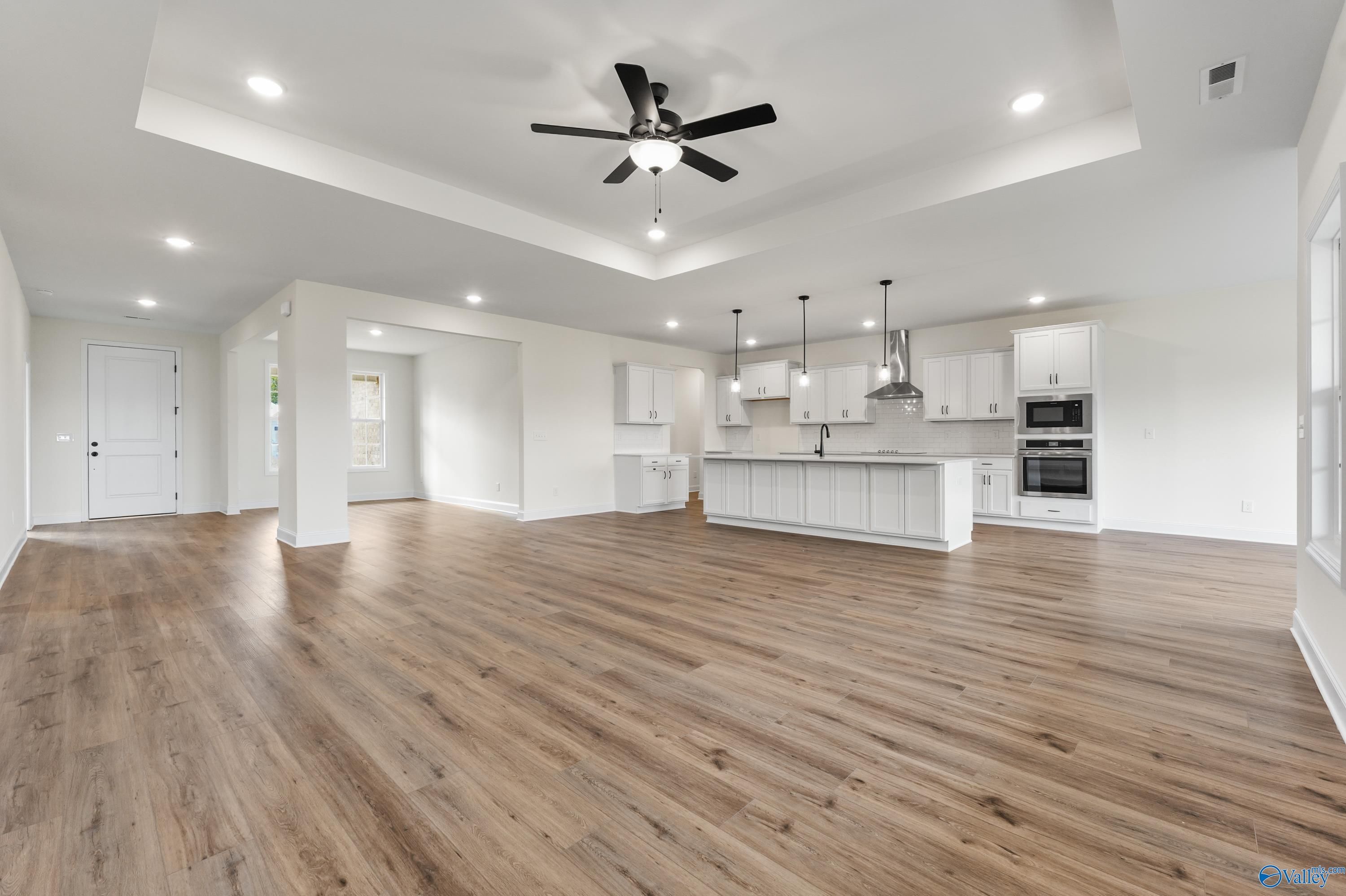 Open-concept kitchen and living area with white cabinetry, central island, ceiling fan, and hardwood floors in Davidson Homes The Finleigh, Harvest AL