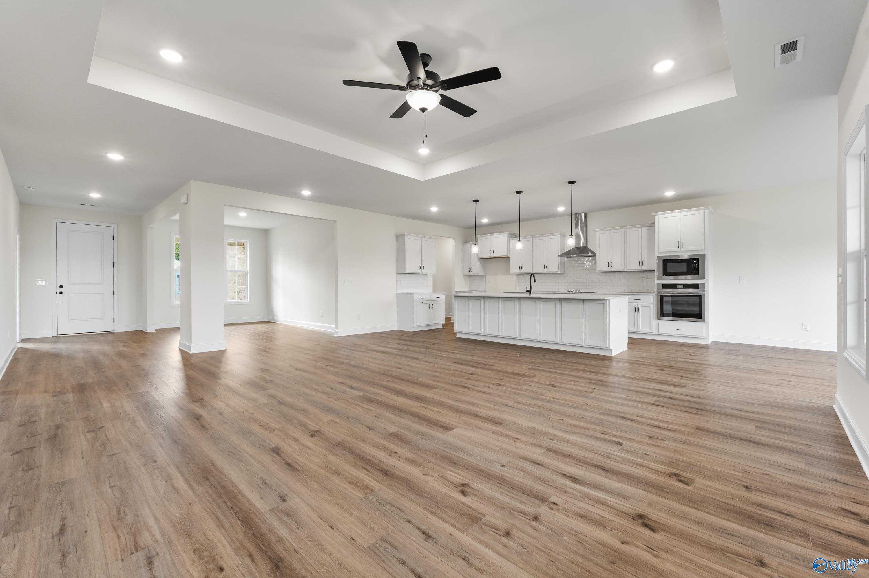 Open-concept kitchen and living area with white cabinetry, central island, ceiling fan, and hardwood floors in Davidson Homes The Finleigh, Harvest AL