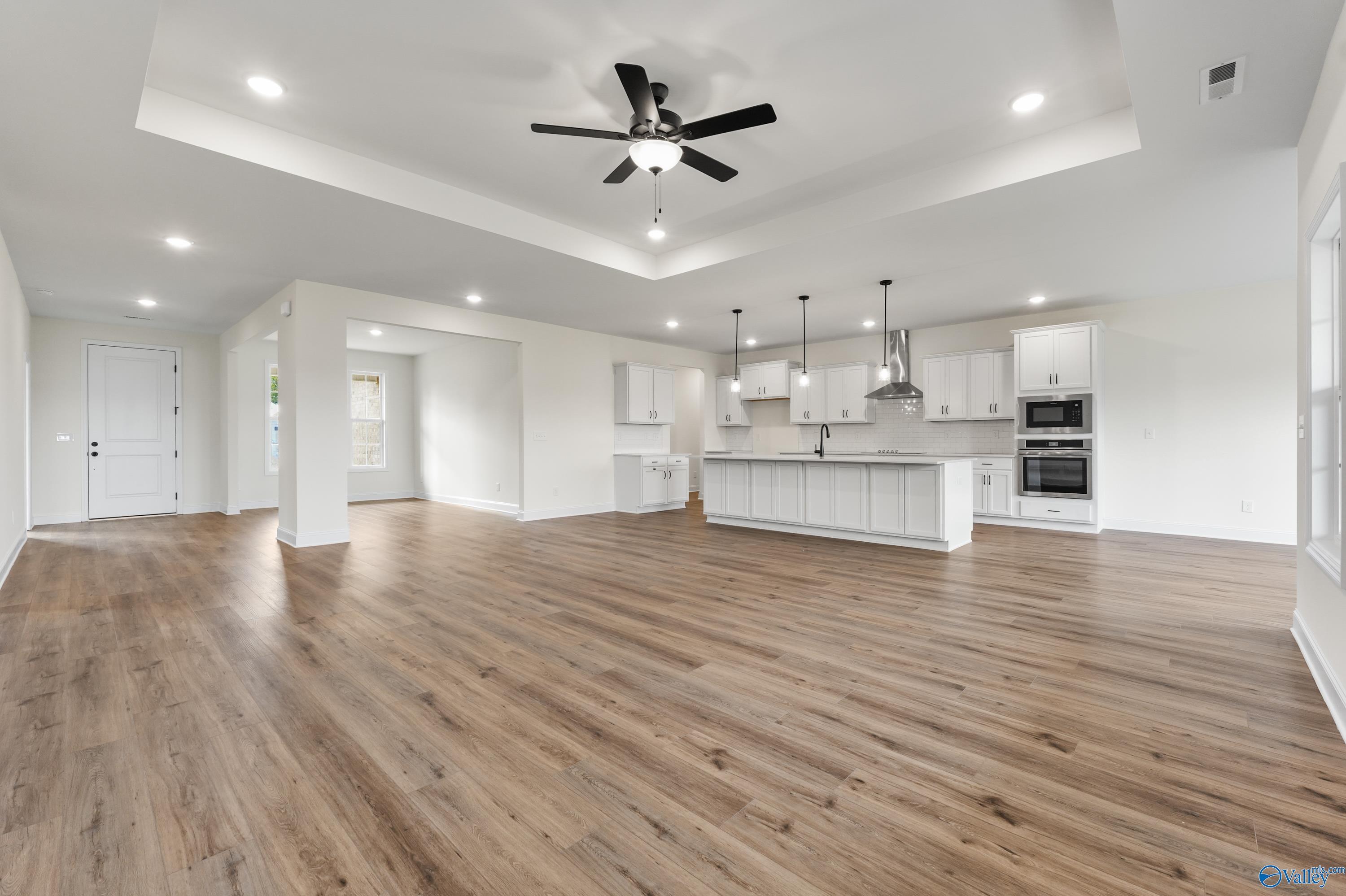 Open-concept kitchen and living area with white cabinetry, central island, ceiling fan, and hardwood floors in Davidson Homes The Finleigh, Harvest AL