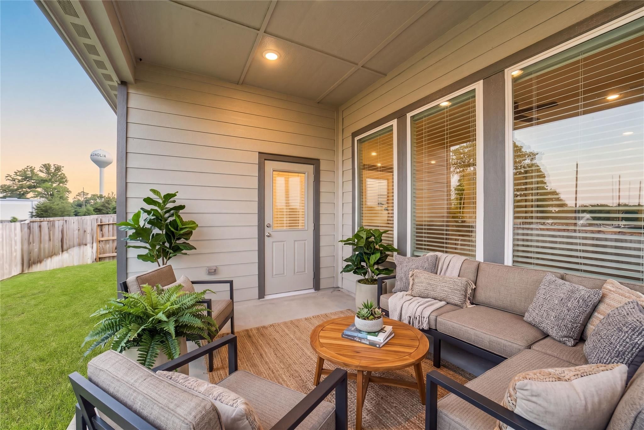 Inviting covered patio with L-shaped beige sectional, wooden coffee table, potted ferns in Davidson Homes The Acadia C, Windmill Estates, Magnolia, Texas