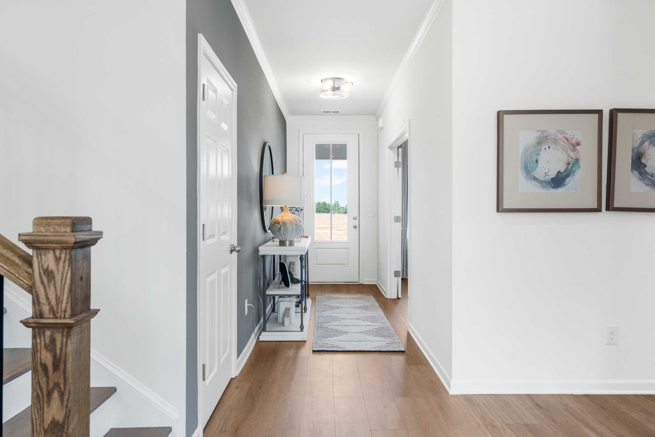 Spacious hallway foyer at Cedar Farms in Winder GA featuring oak staircase, hardwood floors, console table and abstract wall art