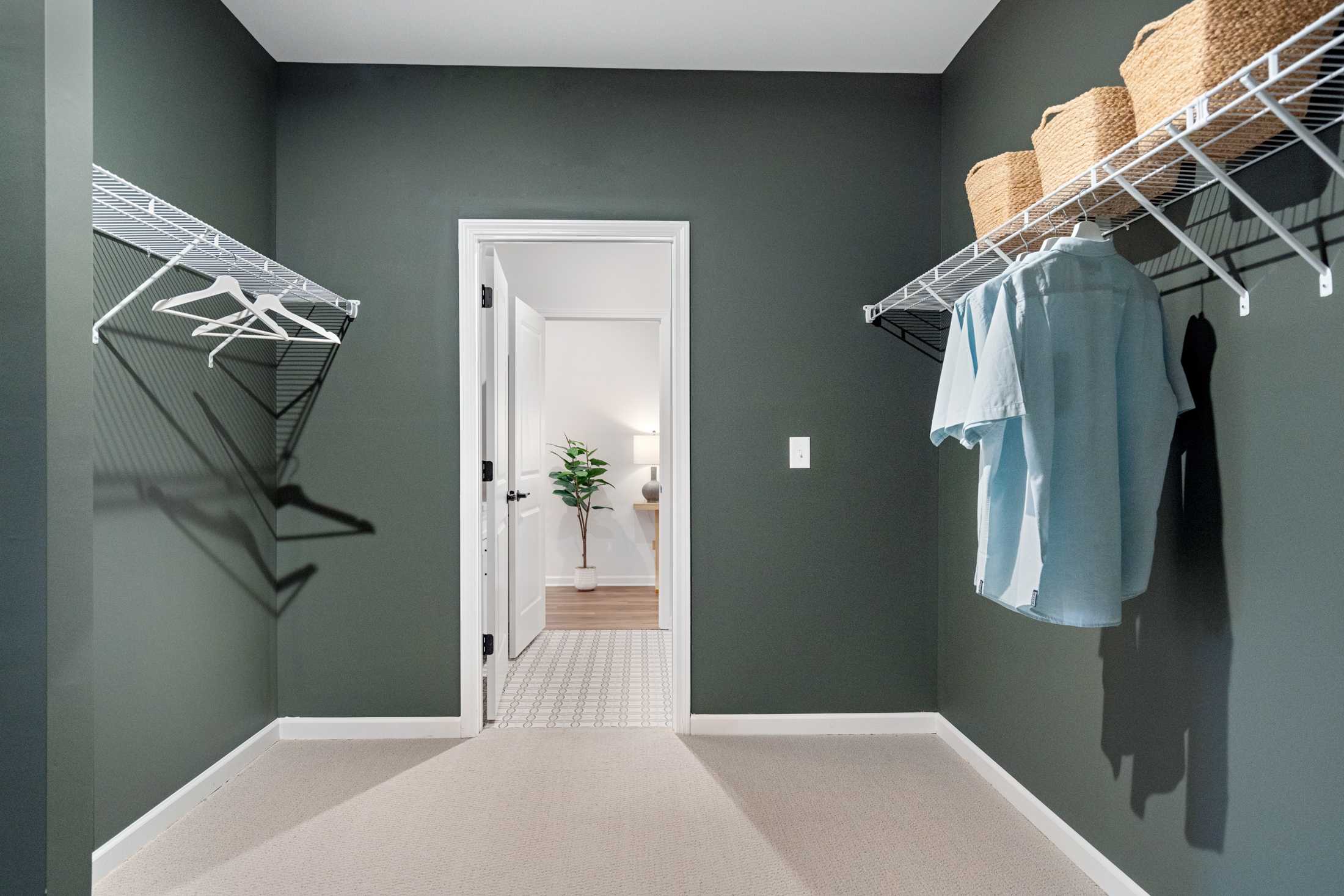 Spacious walk-in closet in The Edison B master suite with sage green walls, wire shelving, woven baskets, and hanging clothes