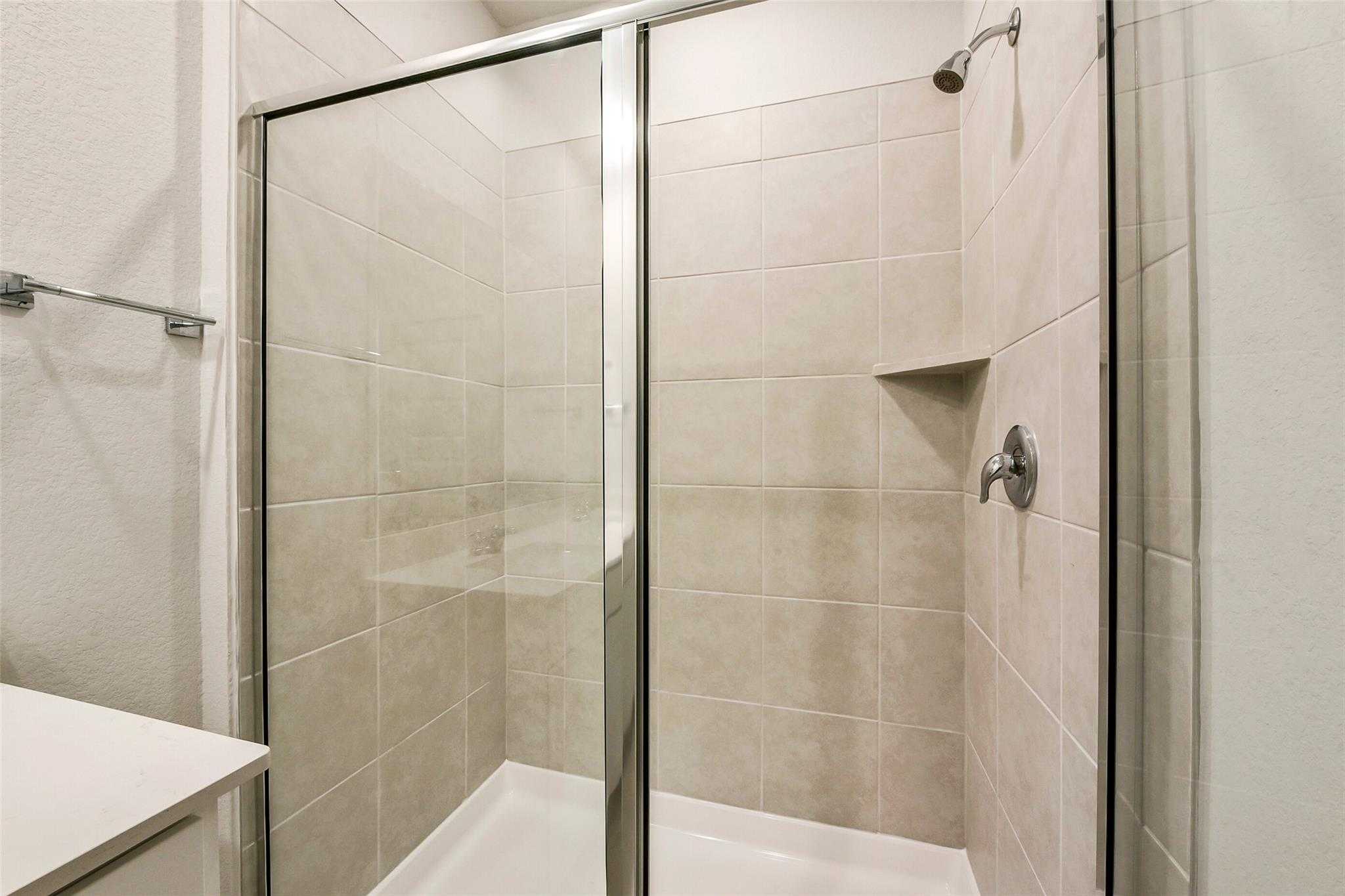 Modern walk-in shower with clear glass door, subway tile walls, and chrome fixtures in master bath of The Comal G home, Dayton, Texas