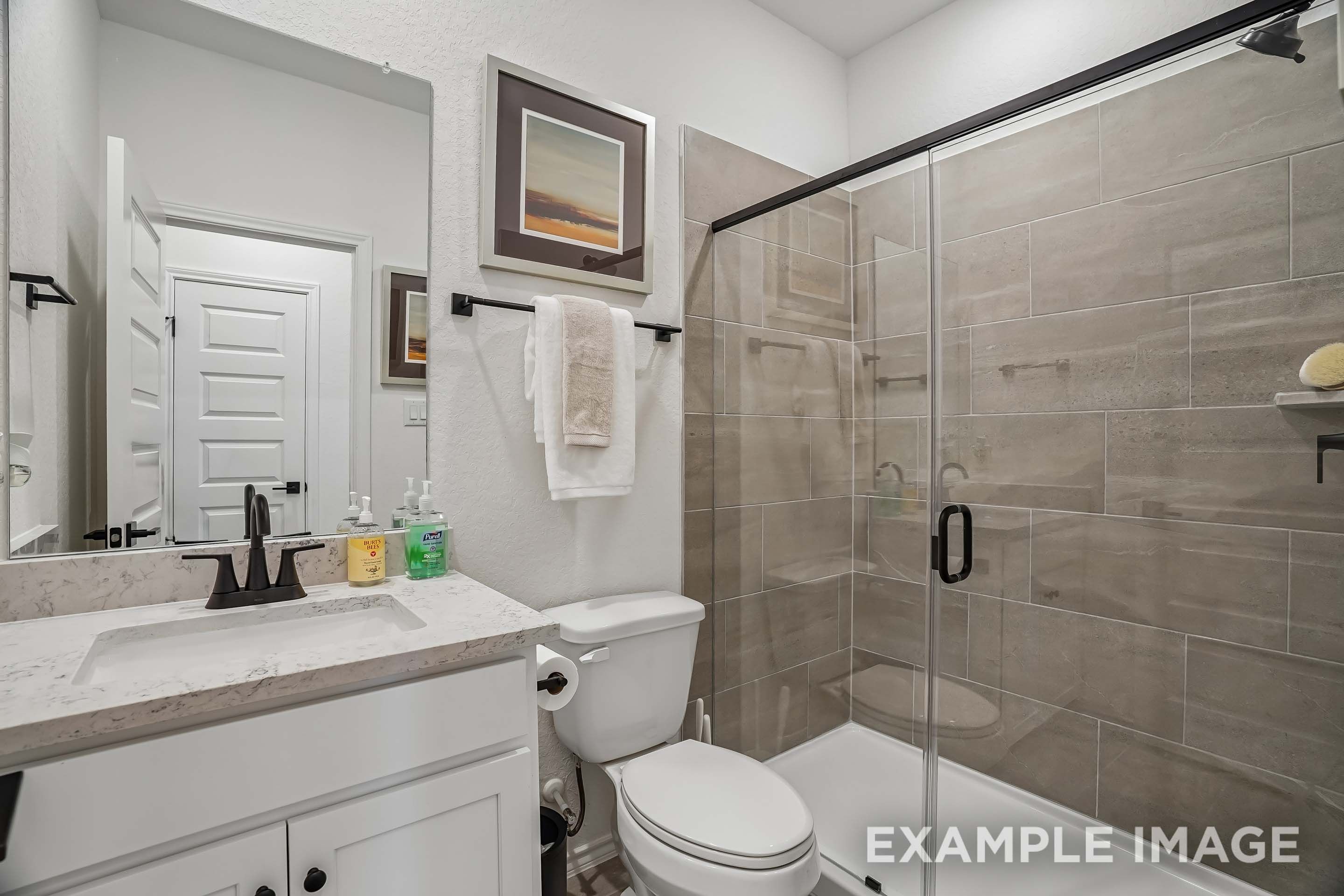 Modern bathroom in The Pinecrest featuring a glass-enclosed tiled shower, quartz vanity, and sleek matte black fixtures.