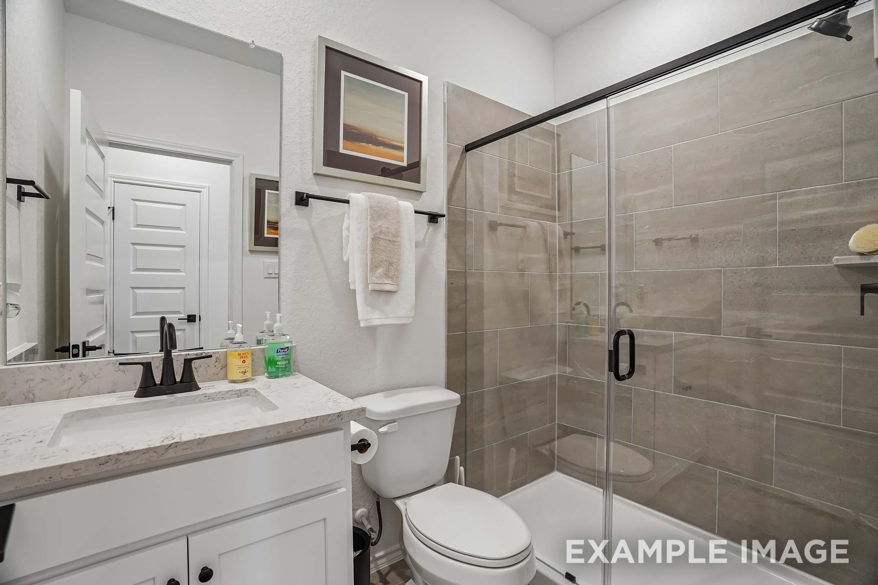 Modern bathroom in The Pinecrest featuring a glass-enclosed tiled shower, quartz vanity, and sleek matte black fixtures.
