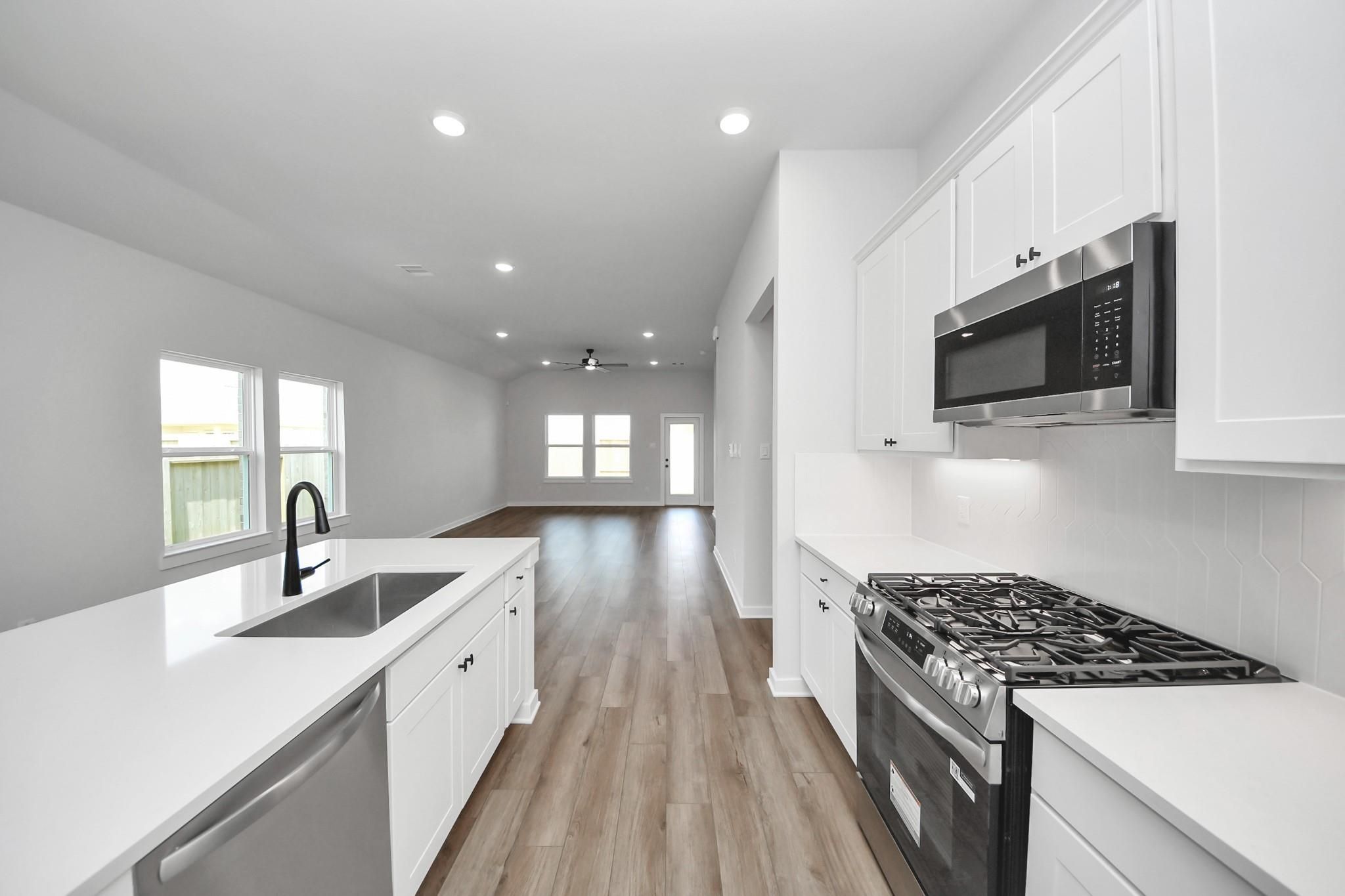 Modern kitchen with white cabinets, quartz countertops, and stainless appliances in The Riviera C plan, Dayton, Texas.