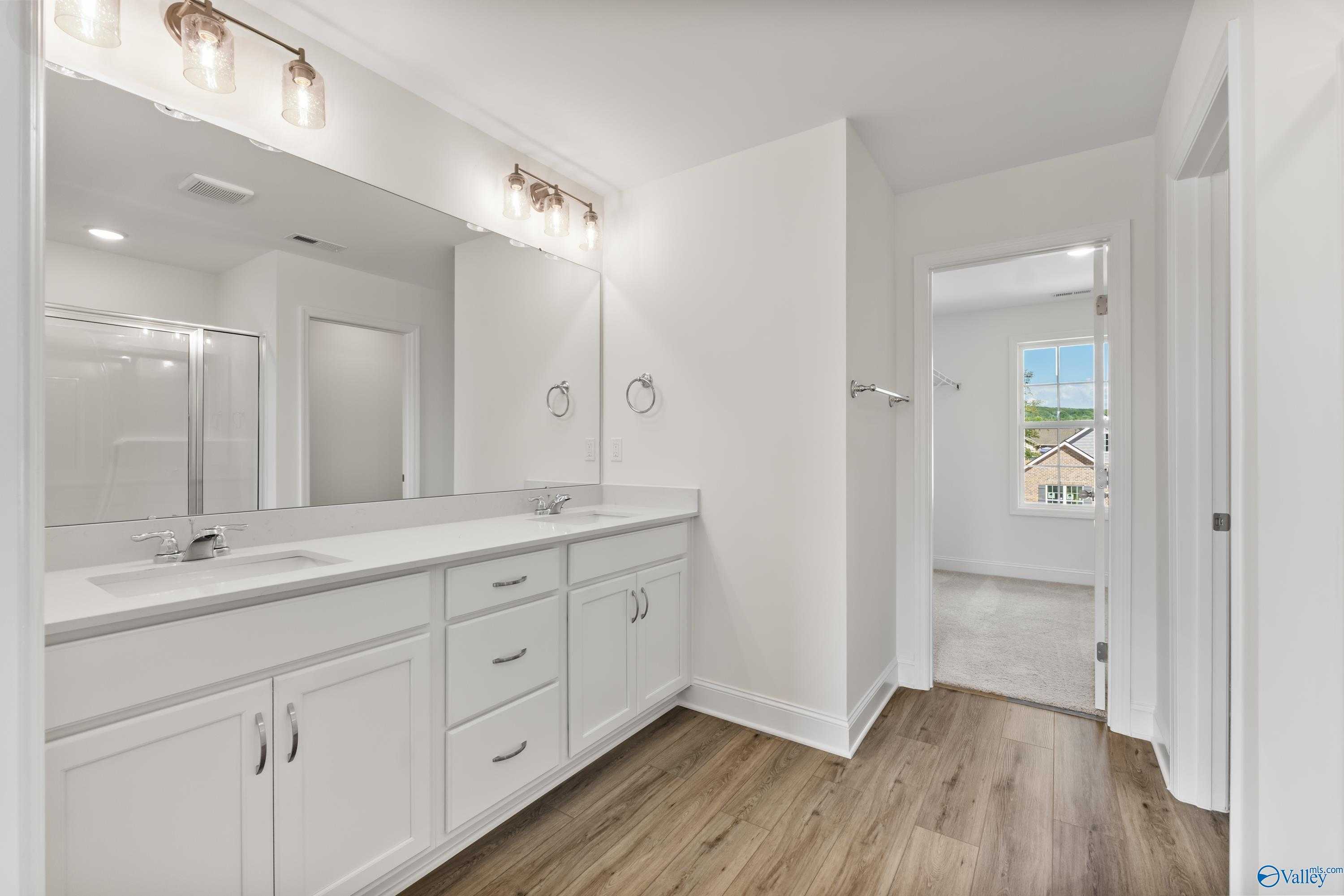 Modern master bathroom with double vanity, white shaker cabinets, glass shower, and luxury vinyl plank flooring in The Shelby A, New Market, AL