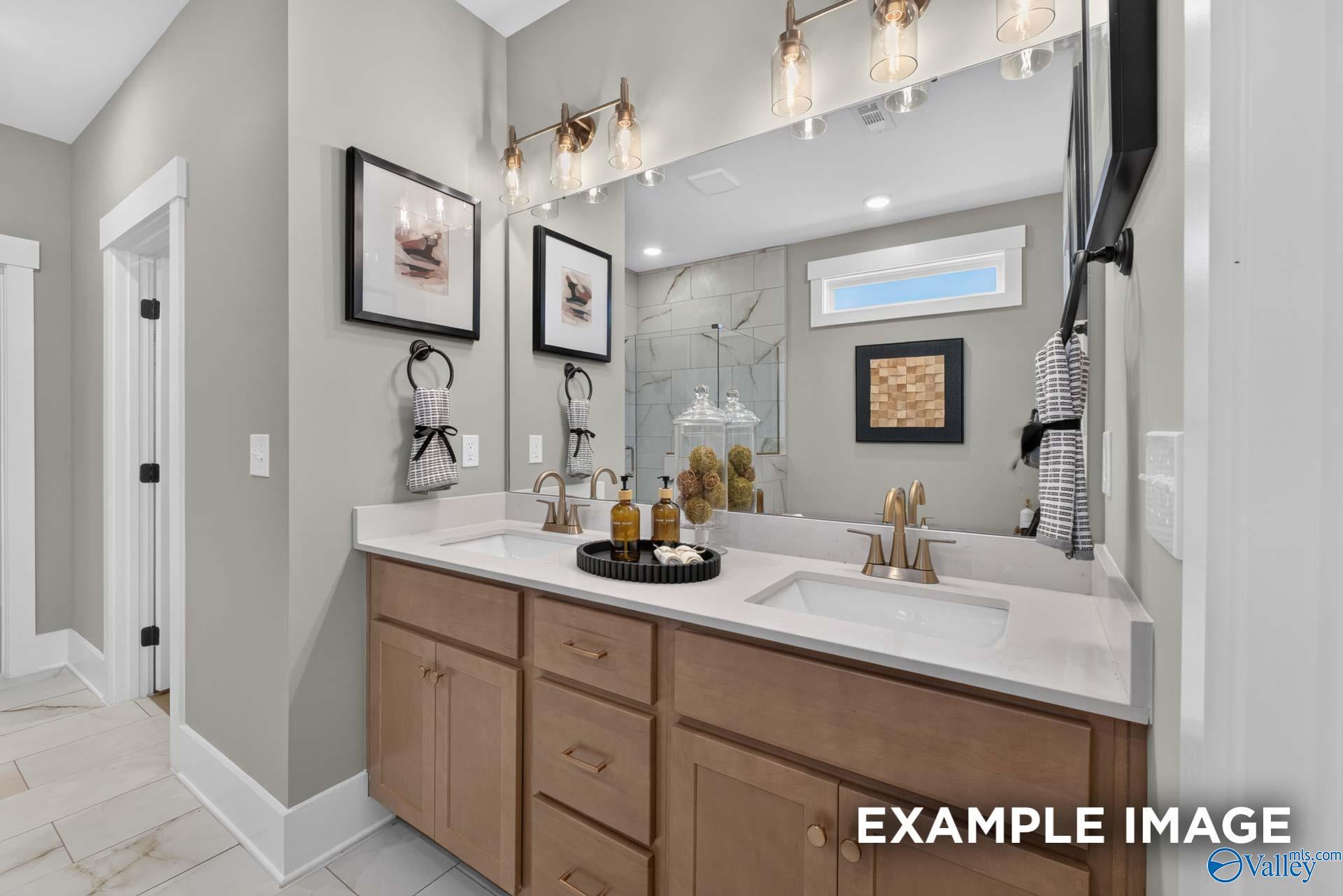 Dual vanity bathroom with wood cabinets, quartz countertops, brass fixtures, and tiled walk-in shower in Davidson Homes Ashport K plan
