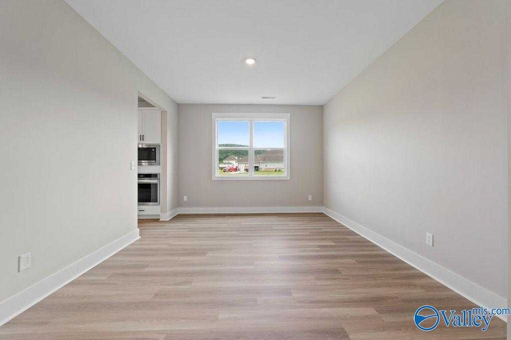 Open-concept great room with light hardwood floors, neutral walls, and large window view adjacent to white kitchen cabinets in Evermore Homes The Oxford, Owens Cross Roads