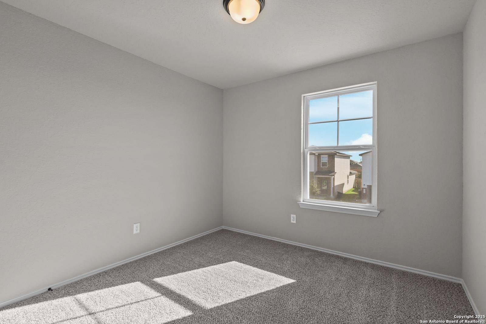 Bright empty bedroom with gray walls, beige carpet, and sunlit window in Davidson Homes The Brazos C, San Antonio