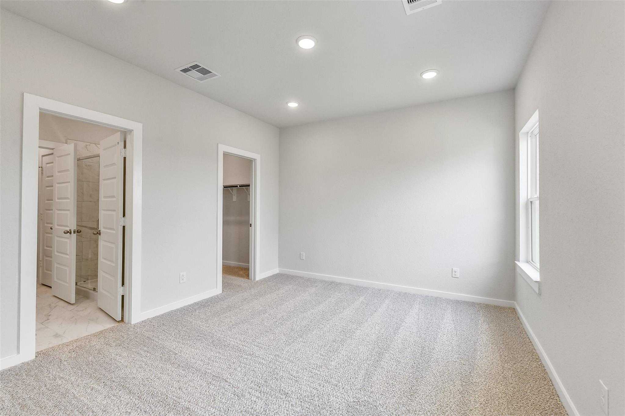 Spacious master bedroom with en-suite bath doors, walk-in closet, carpeted floor in Davidson Homes The Colorado G, Magnolia, Texas