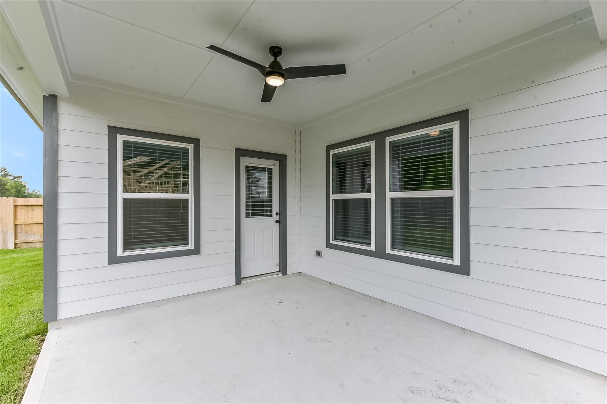 Covered patio with black ceiling fan, white exterior, gray-trimmed windows and door in Davidson Homes The Everett C, Crosby TX