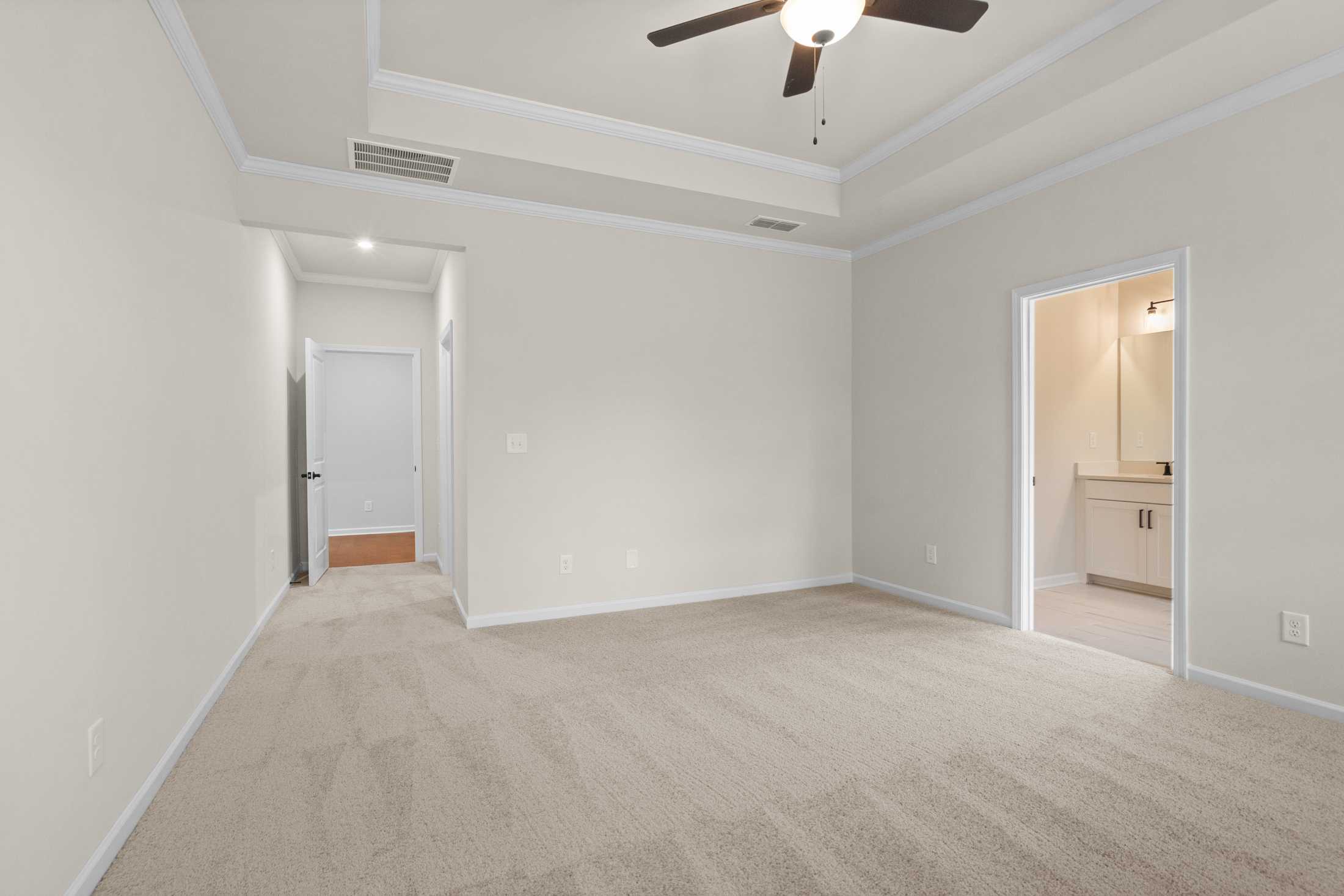 Spacious master bedroom in The Glenwood B featuring beige carpet, tray ceiling fan, en-suite bath with vanity