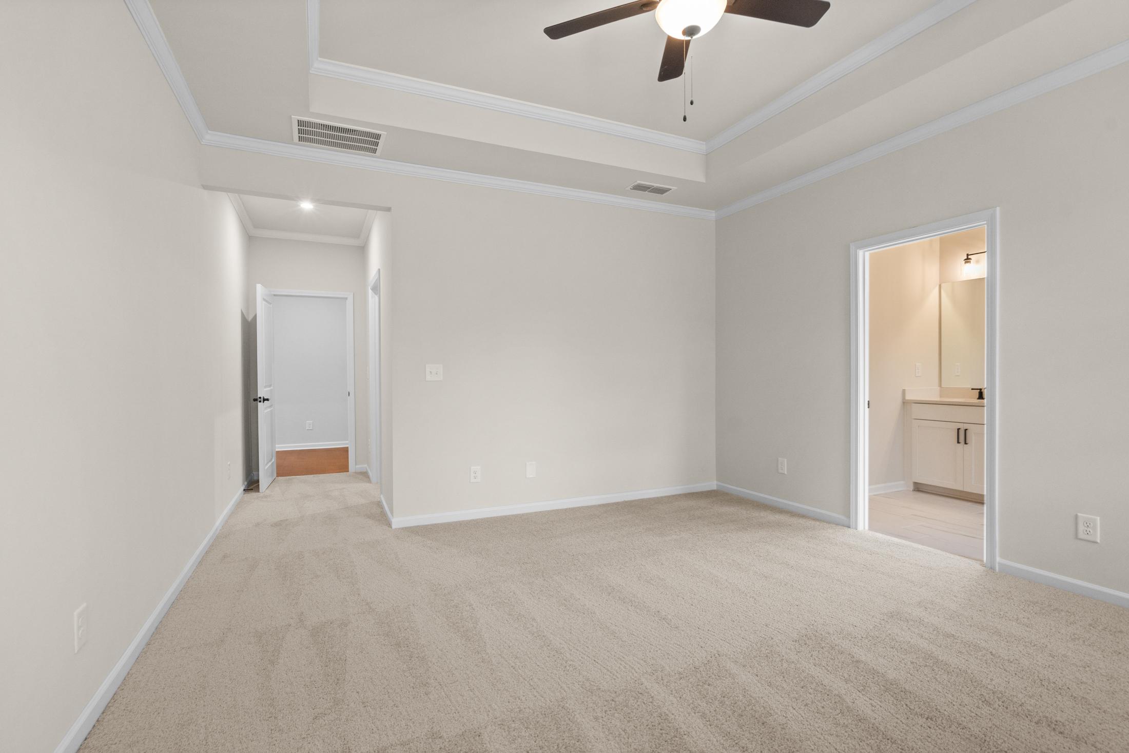 Spacious master bedroom in The Glenwood with tray ceiling, ceiling fan, beige carpet, and en-suite bath access