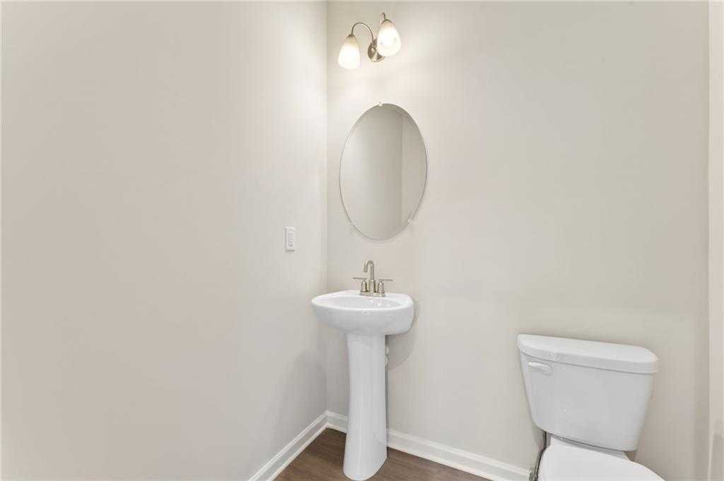 Elegant half bathroom featuring white pedestal sink, round mirror, wall sconces, and toilet in Davidson Homes The Ash B, Riverwood, Dallas, Georgia