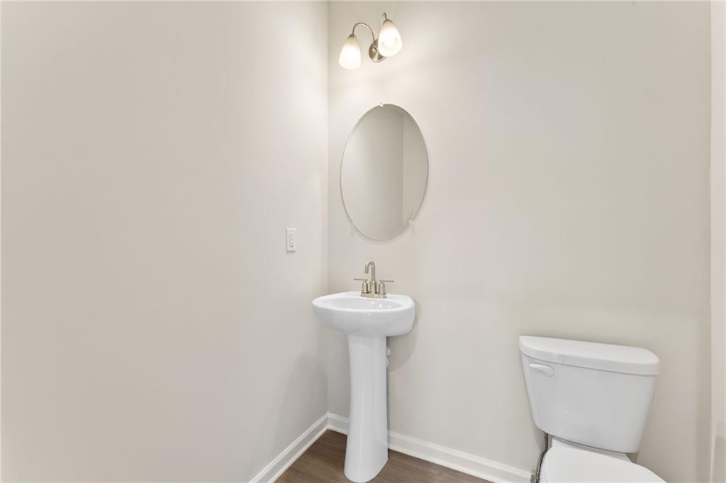 Elegant powder room with white pedestal sink, round mirror, and sconce lights in Davidson Homes The Ash B plan, Riverwood, Dallas, GA