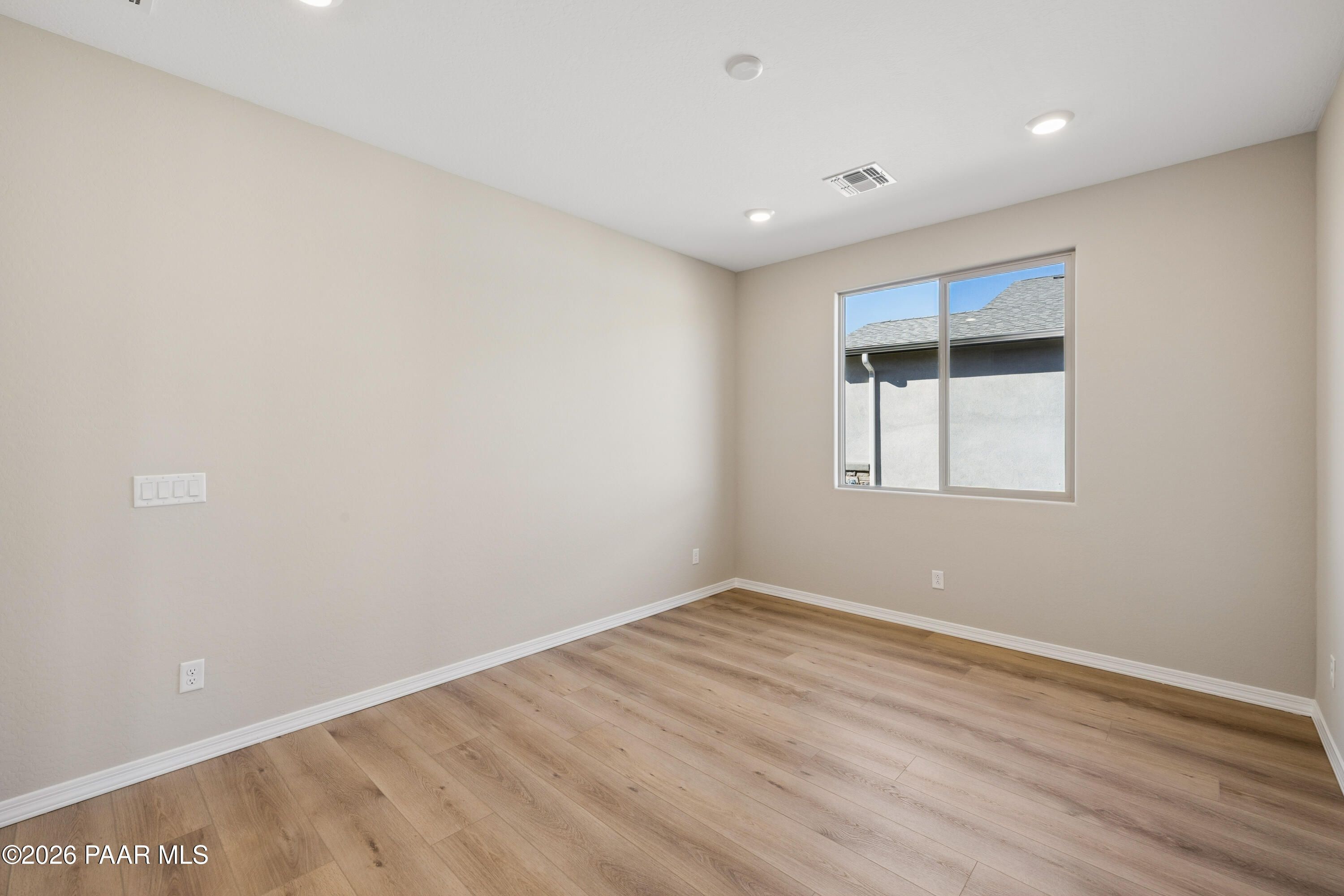 Bright secondary bedroom with beige walls, luxury vinyl plank flooring, and large window in Davidson Homes The Harmony A, Prescott Valley, AZ