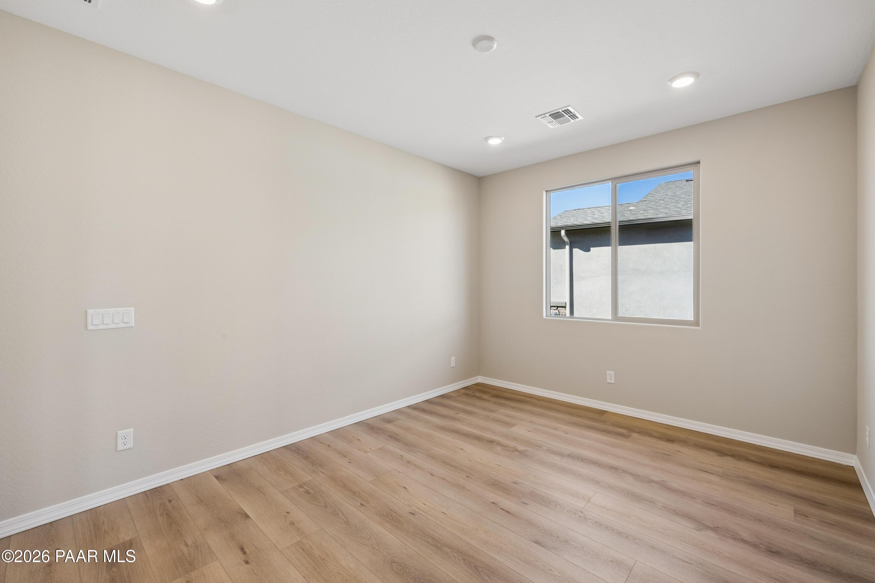 Bright secondary bedroom with beige walls, luxury vinyl plank flooring, and large window in Davidson Homes The Harmony A, Prescott Valley, AZ