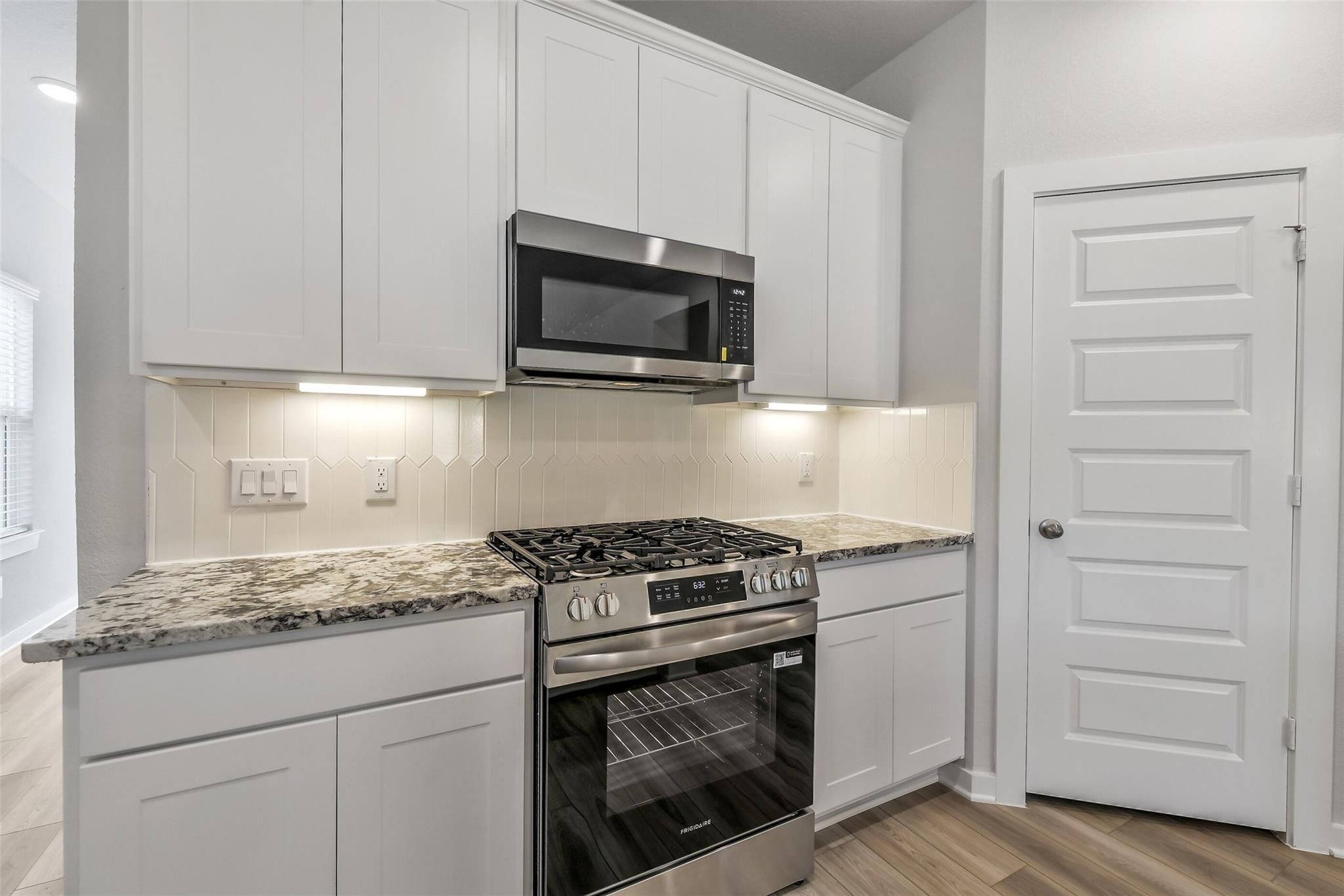 Modern white shaker kitchen with granite counters, gas cooktop, stainless Frigidaire oven, and under-cabinet lighting in San Marcos E home, Conroe, TX