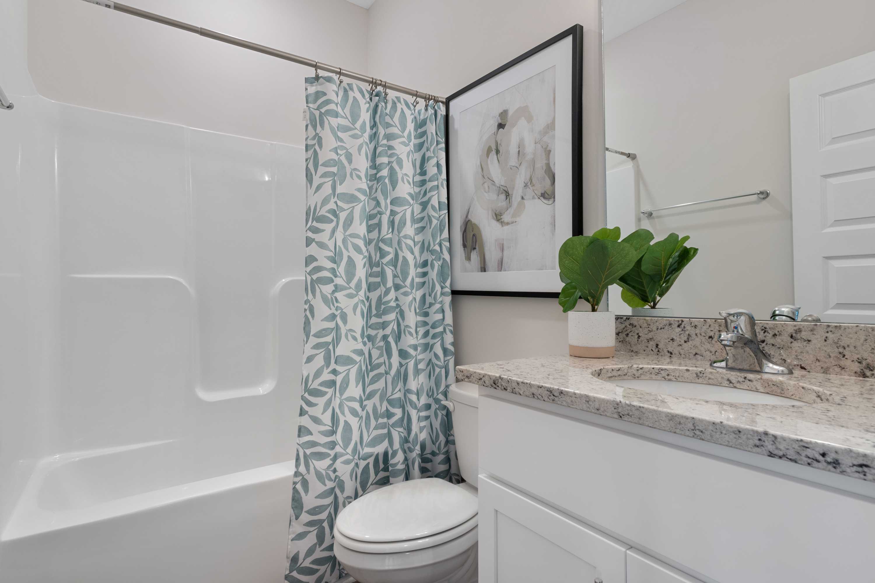Spacious bathroom at The Retreat at Cain Park in Hartselle Alabama with white tub, blue leaf shower curtain, granite vanity and potted plant