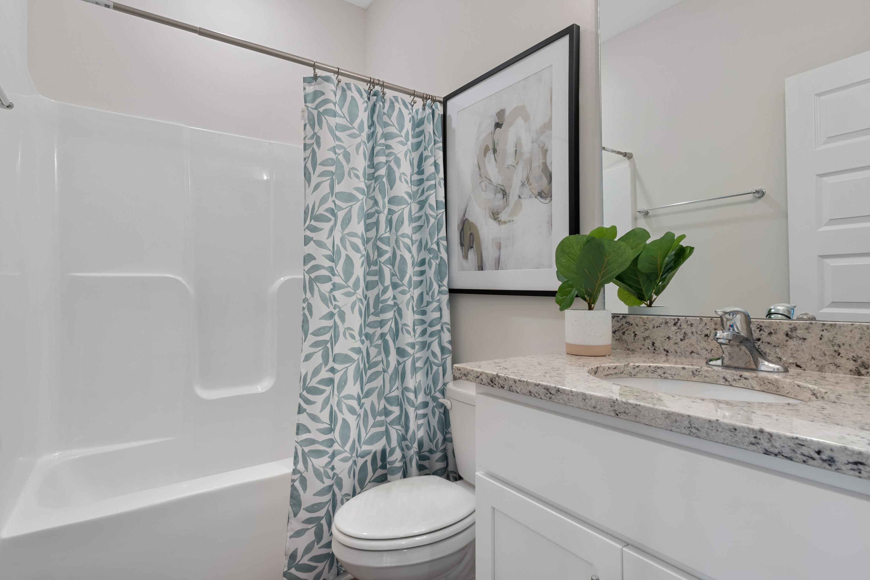Spacious bathroom at The Retreat at Cain Park in Hartselle Alabama with white tub, blue leaf shower curtain, granite vanity and potted plant