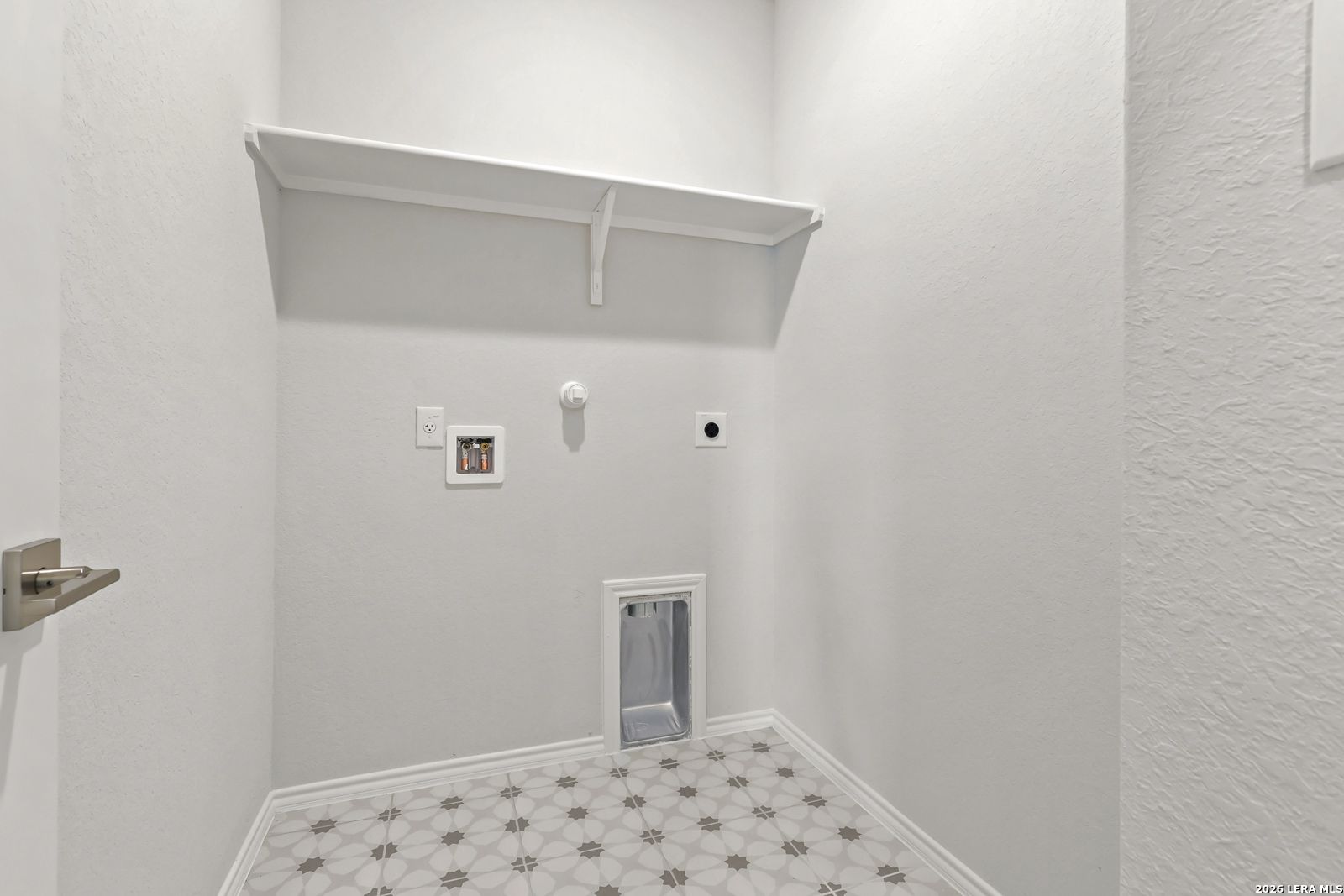 Laundry room with white shelving, washer connections, and patterned tile floor in Davidson Homes The Daphne I, Bricewood San Antonio