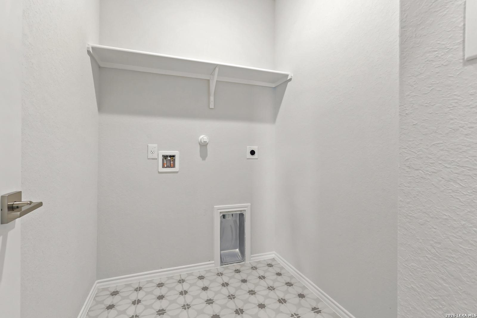 Laundry room with white shelving, washer connections, and patterned tile floor in Davidson Homes The Daphne I, Bricewood San Antonio
