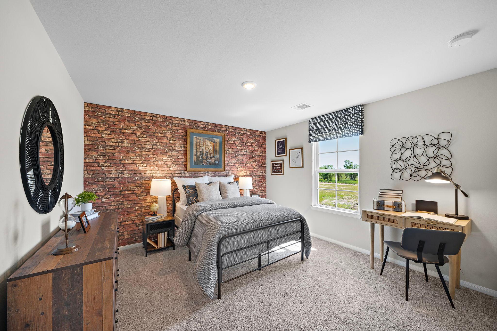 Cozy bedroom at Emberly in Beasley Texas featuring exposed brick accent wall, gray metal bed, desk workspace and window view