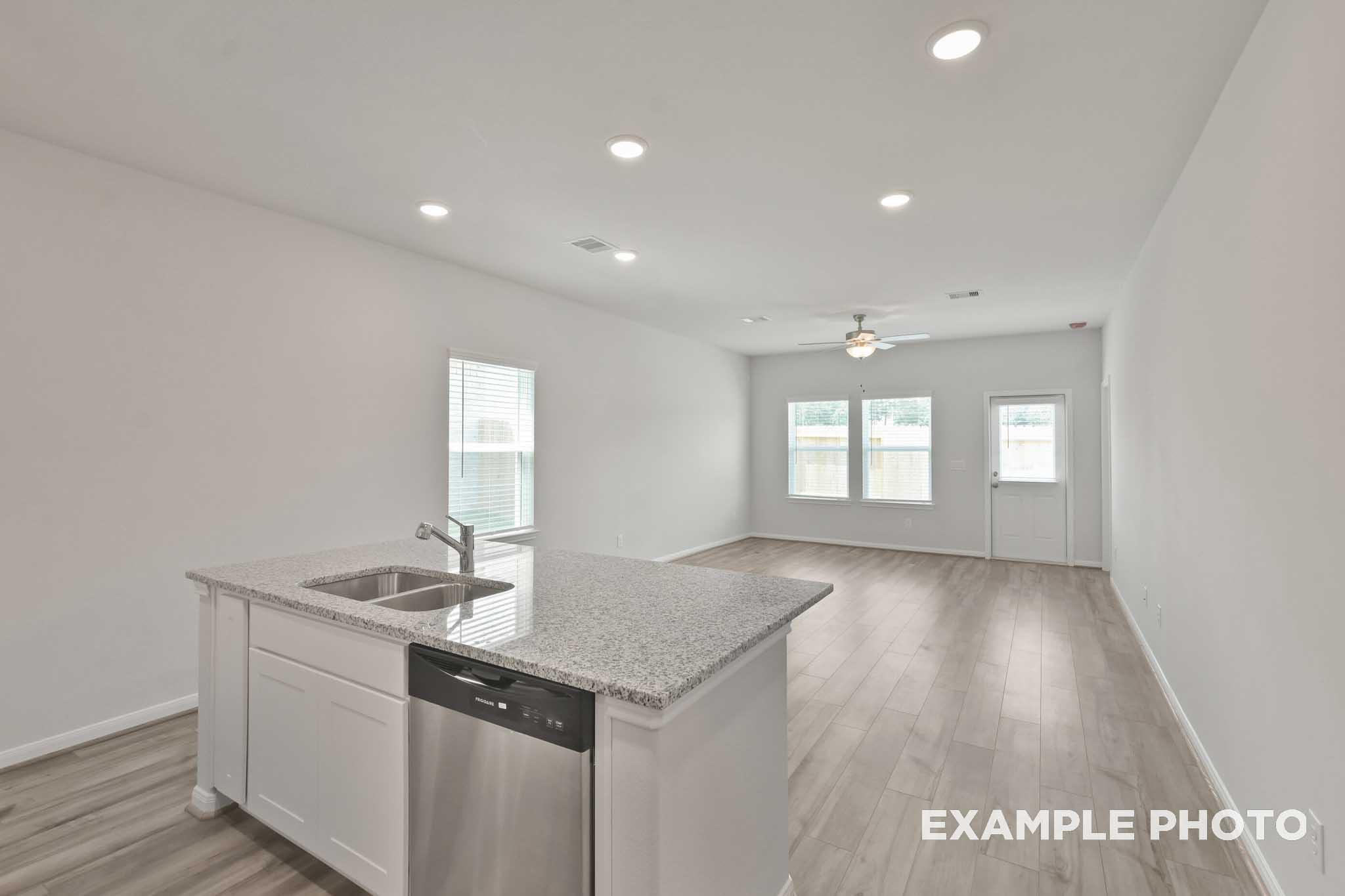 Open-concept kitchen in The Comal floor plan with granite island, sink, white cabinets, dishwasher, and hardwood floors