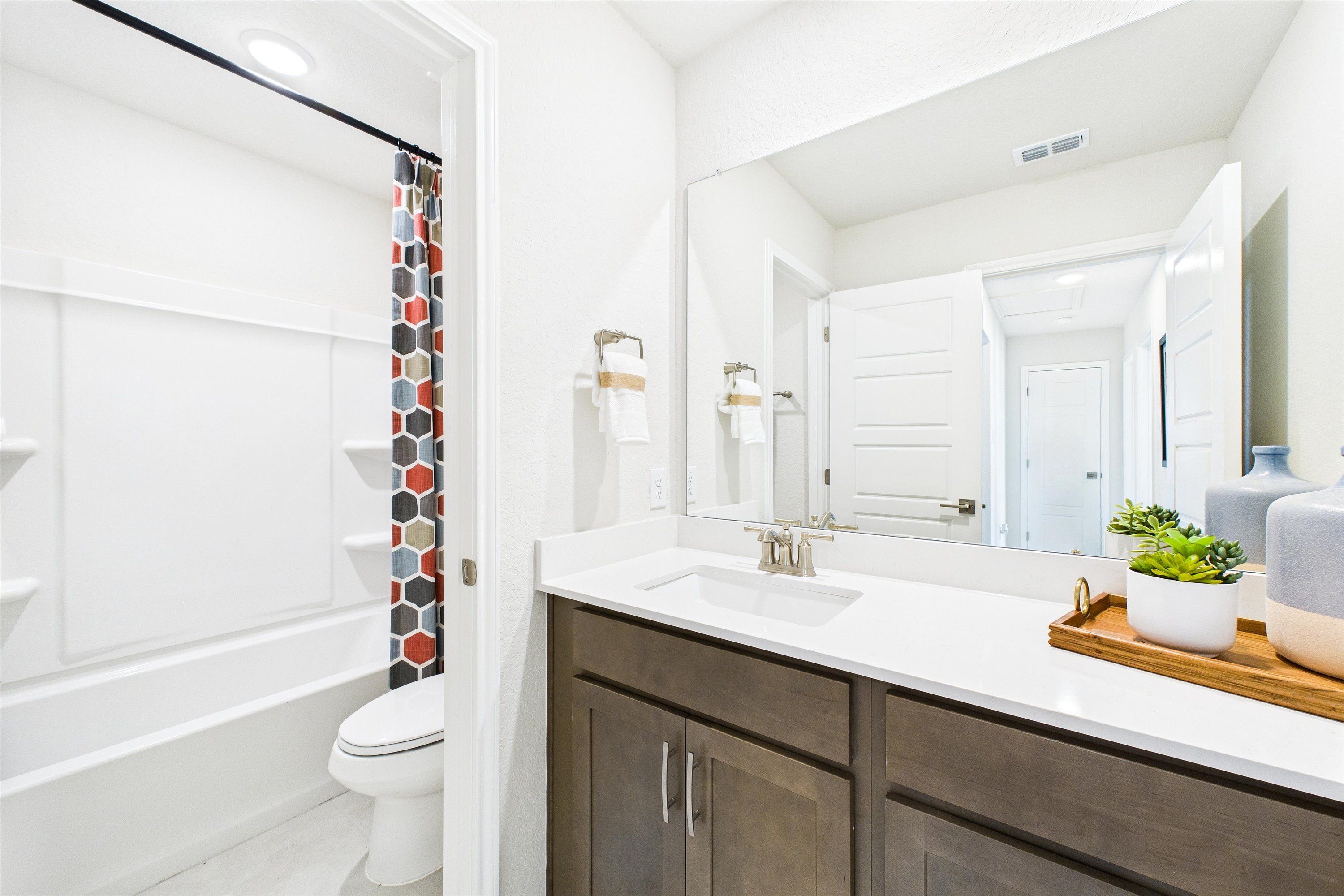 Spacious modern bathroom in Agave San Antonio TX by Davidson Homes with white subway tile shower, soaking tub, dark wood vanity, and potted succulents
