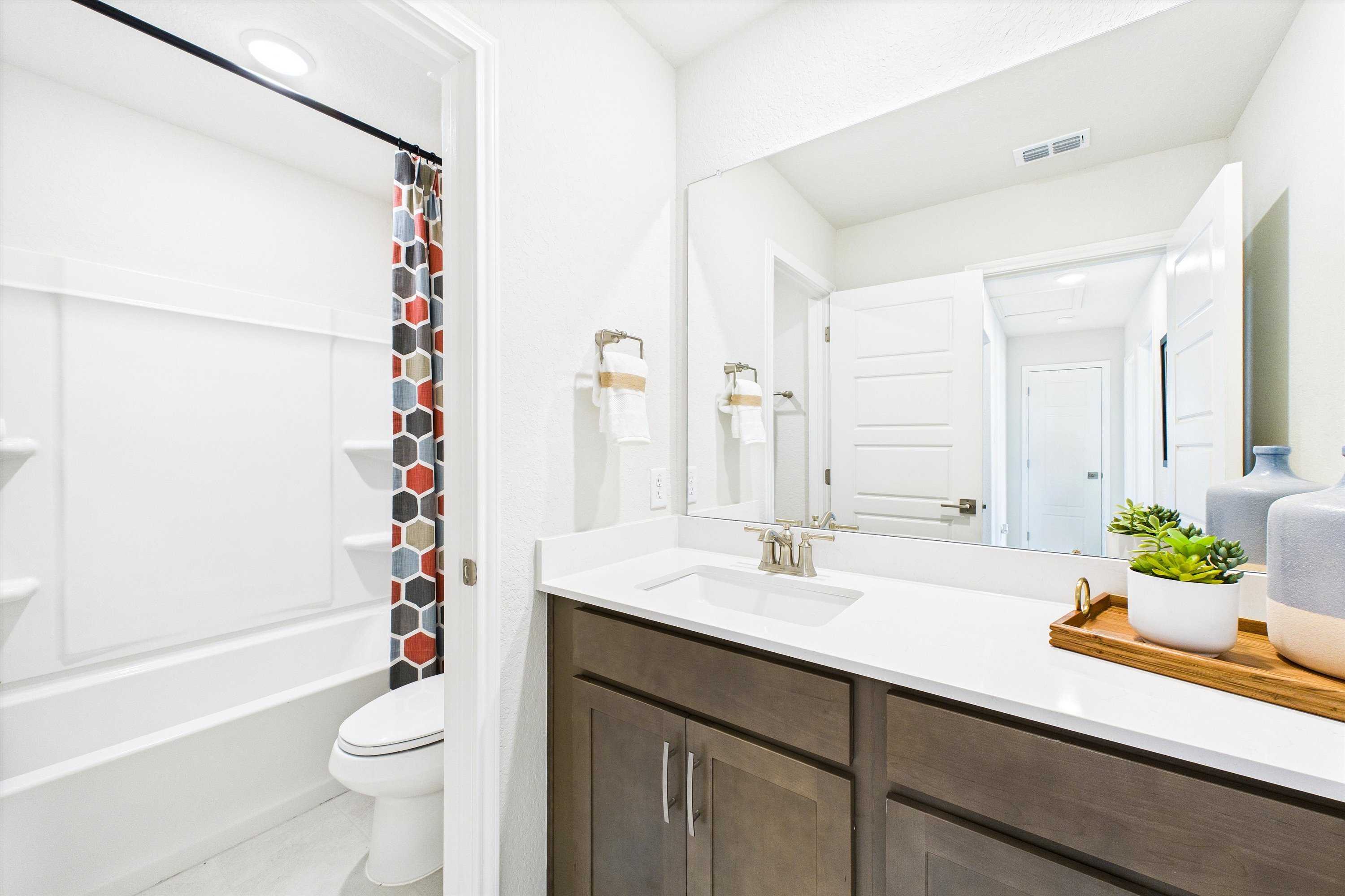 Spacious modern bathroom in Agave San Antonio TX by Davidson Homes with white subway tile shower, soaking tub, dark wood vanity, and potted succulents