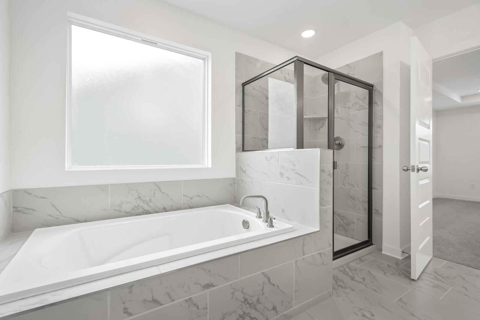 Elegant master bathroom with soaking tub, glass shower, and marble tiles in Davidson Homes The Gordon C, White House, TN
