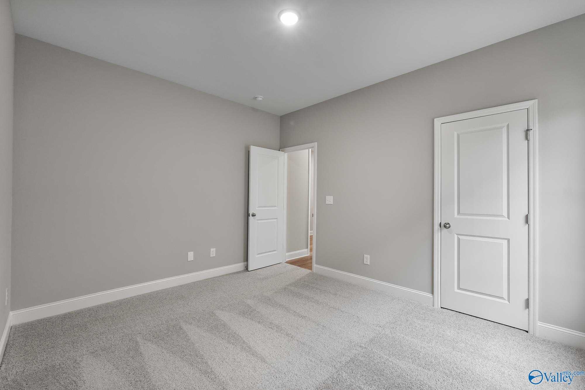 Spacious empty bedroom with light gray walls, white doors, and carpet in Davidson Homes The Daphne D, Athens, Alabama