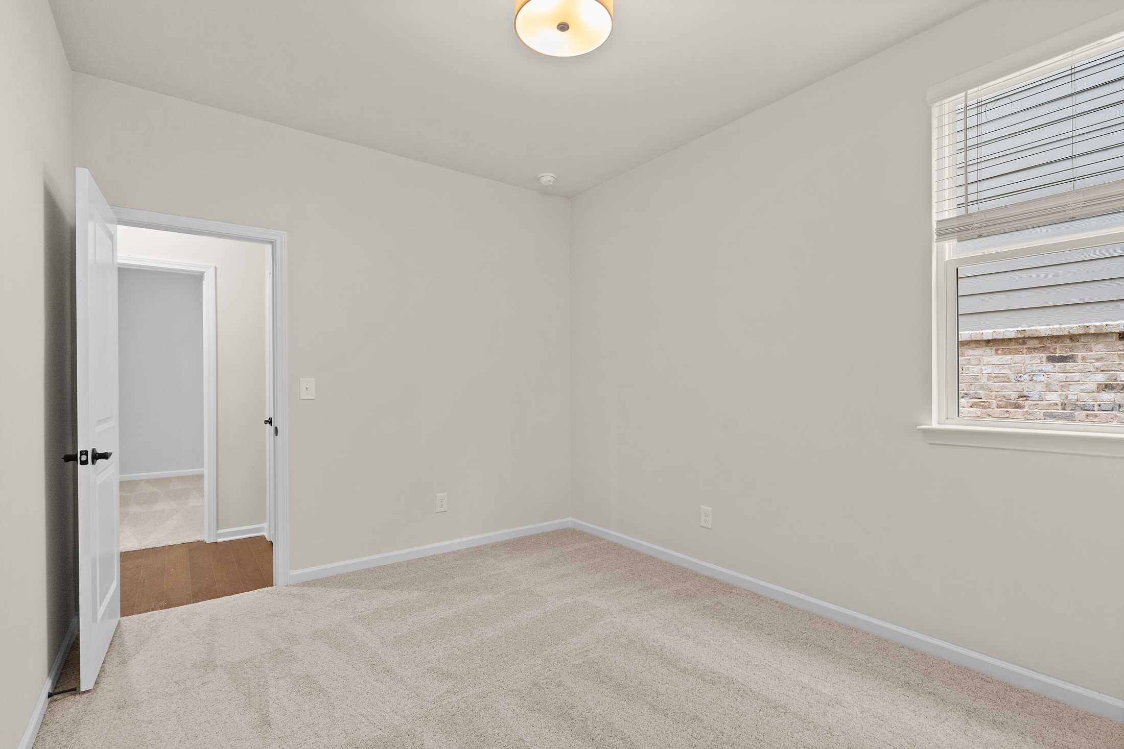Spacious secondary bedroom in The Glenwood B with neutral walls, beige carpet, open doorway, and window blinds