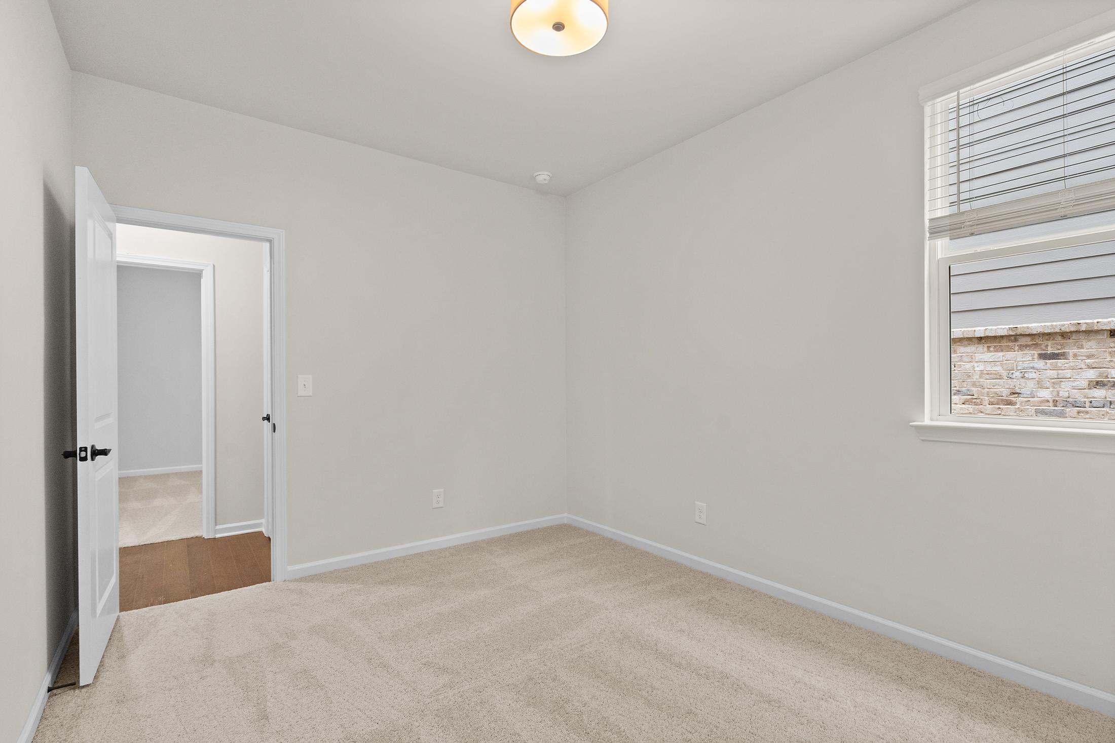 Spacious secondary bedroom in The Glenwood with neutral beige walls, plush carpet, open doorway, and window blinds