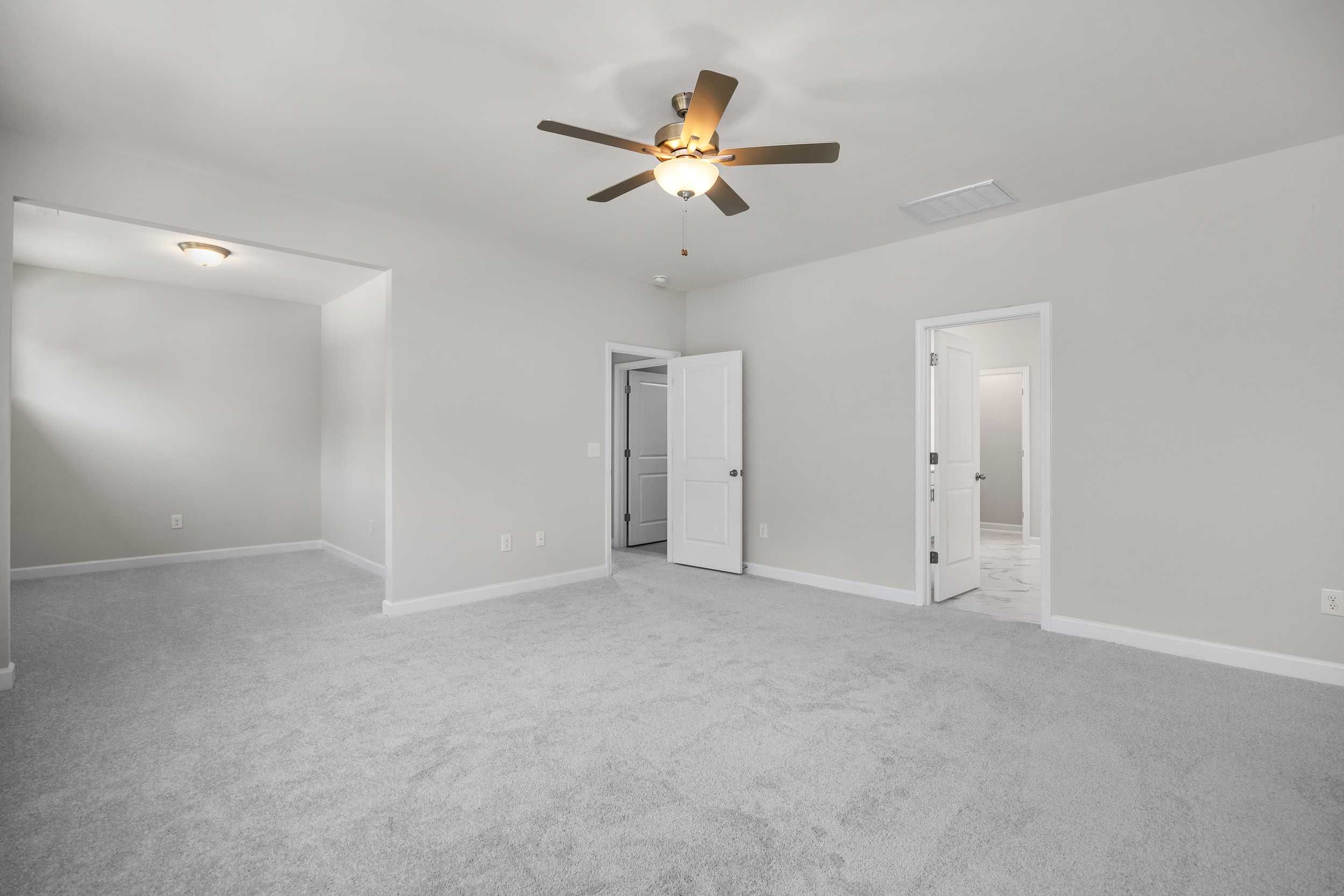 Spacious upper-floor master suite in The Aspen C with neutral gray walls, beige carpet, ceiling fan, and double doorways