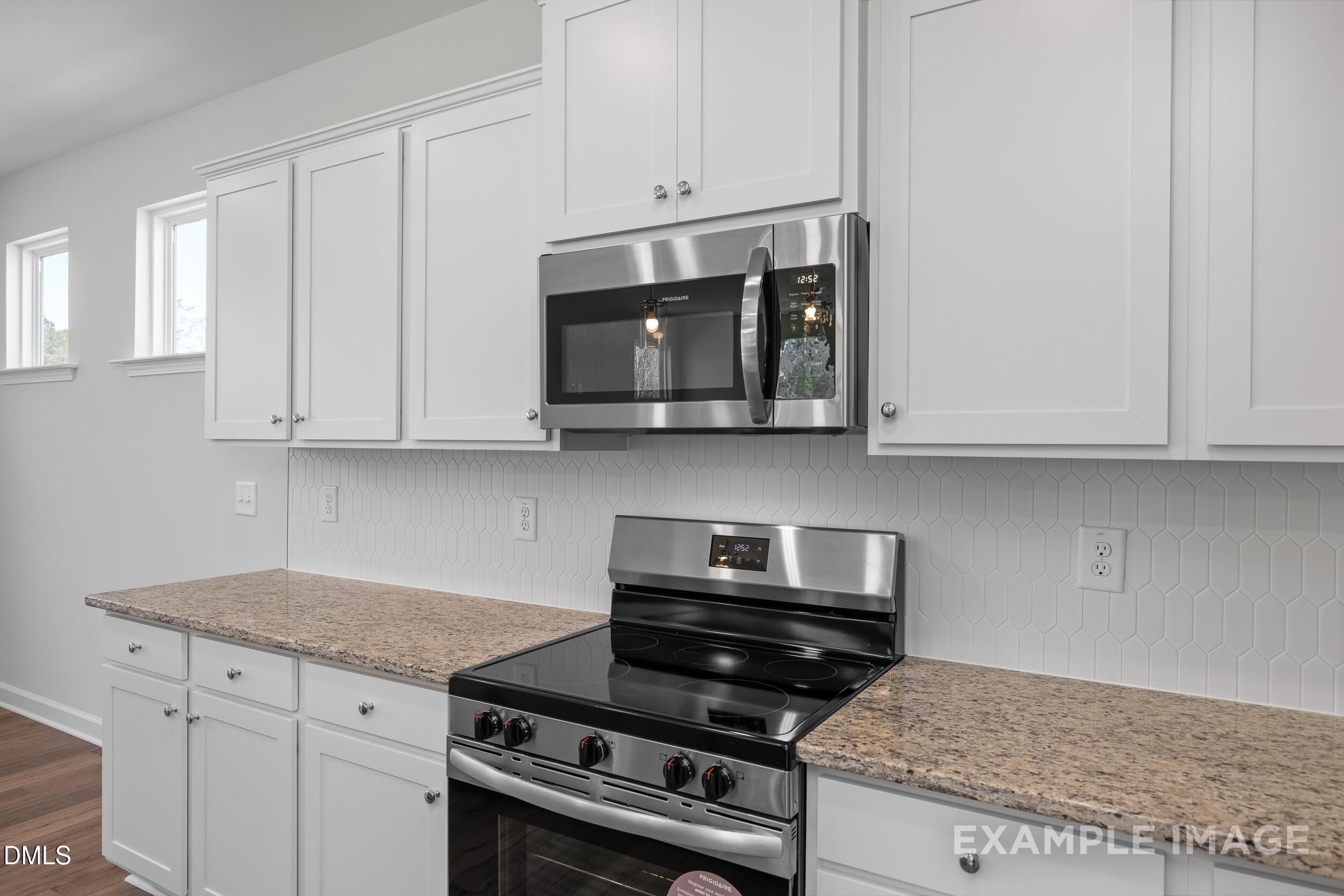 Modern kitchen with white cabinets, granite countertops, and stainless steel appliances in The Gavin A, Gregory Village.