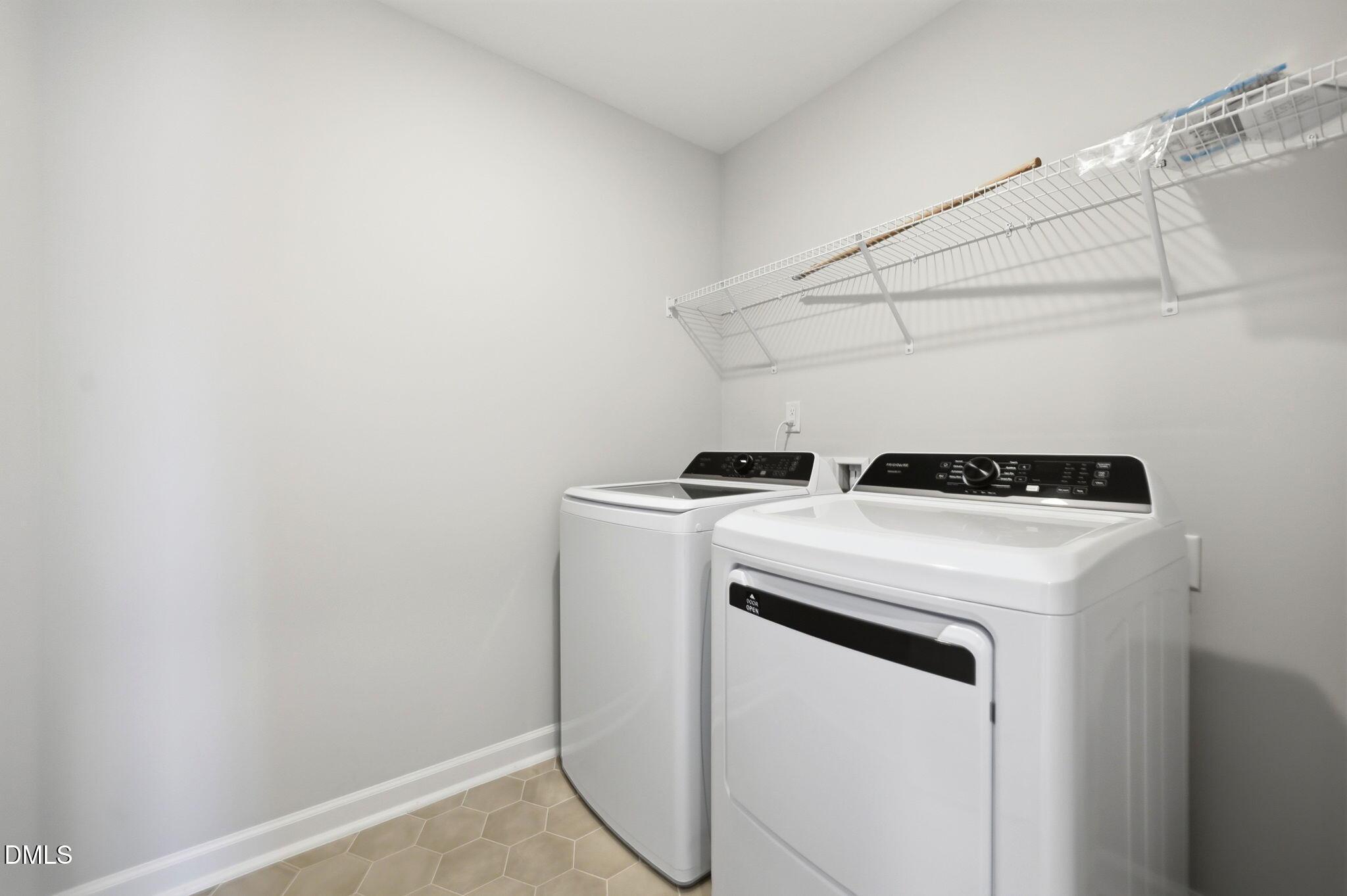 Laundry room with white washer and dryer, tile flooring, and wire shelving in Davidson Homes Avery floor plan, Knightdale.