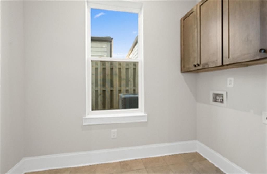 Bright laundry room with wooden cabinets, washer-dryer hookups, and window overlooking fenced backyard in Davidson Homes Seaside A, Woodstock, GA