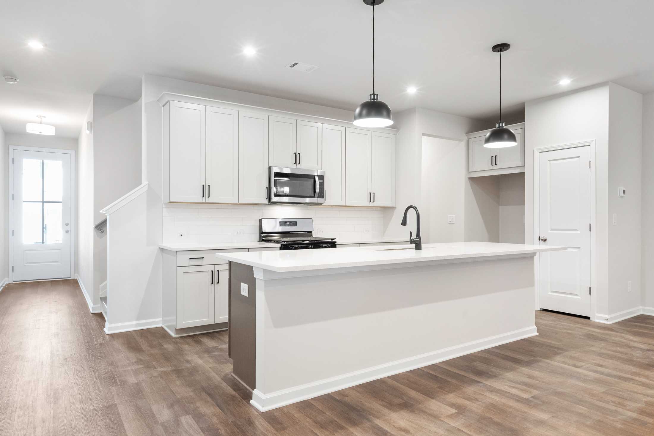 Modern kitchen in The Cary B by Davidson Homes featuring white shaker cabinets, large island with sink, and stainless appliances