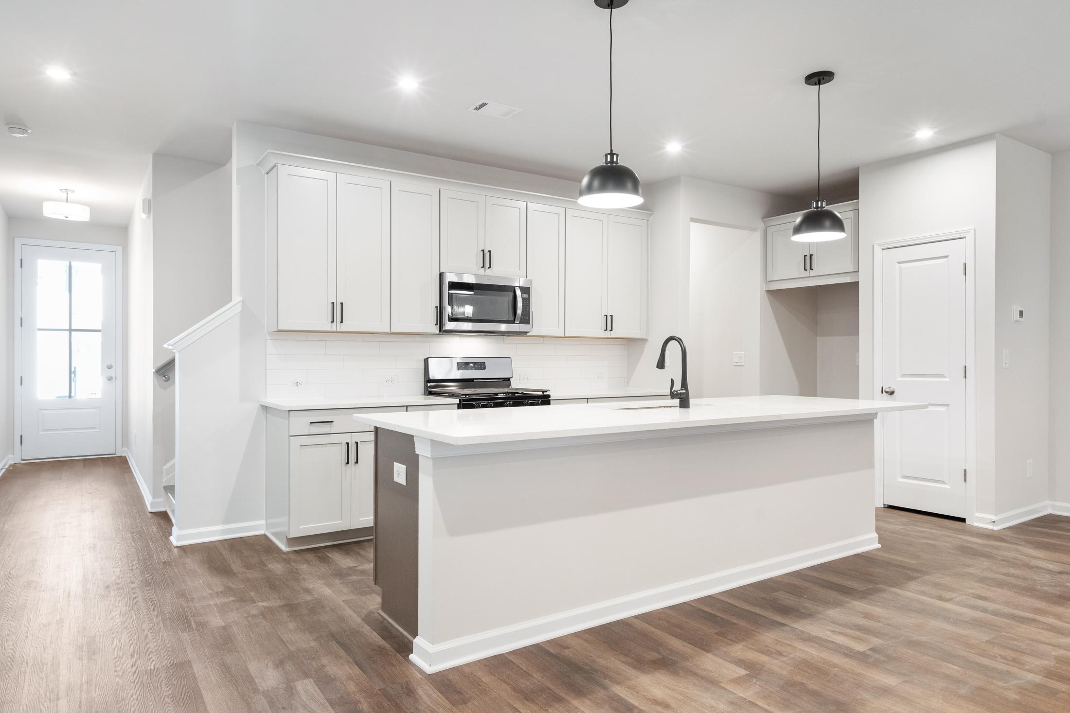 Modern kitchen in The Cary B by Davidson Homes featuring white shaker cabinets, large island with sink, and stainless appliances