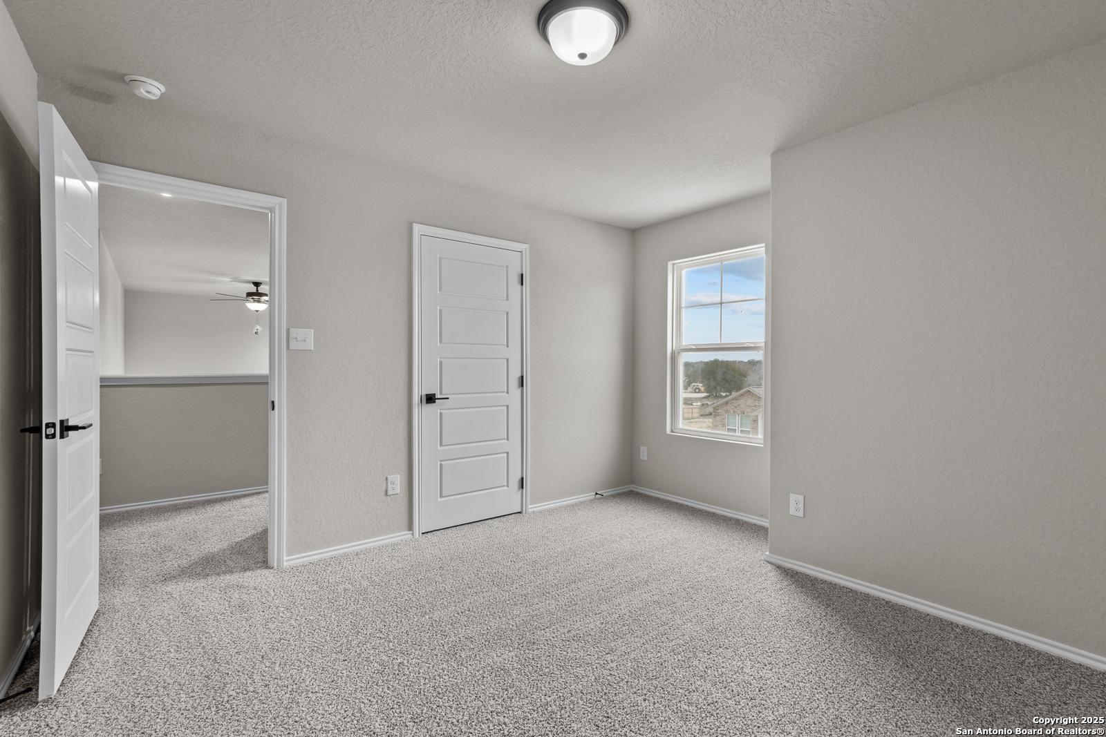 Bright secondary bedroom with neutral walls, carpet flooring, ceiling fan, and window view in Davidson Homes The Murray I, San Antonio