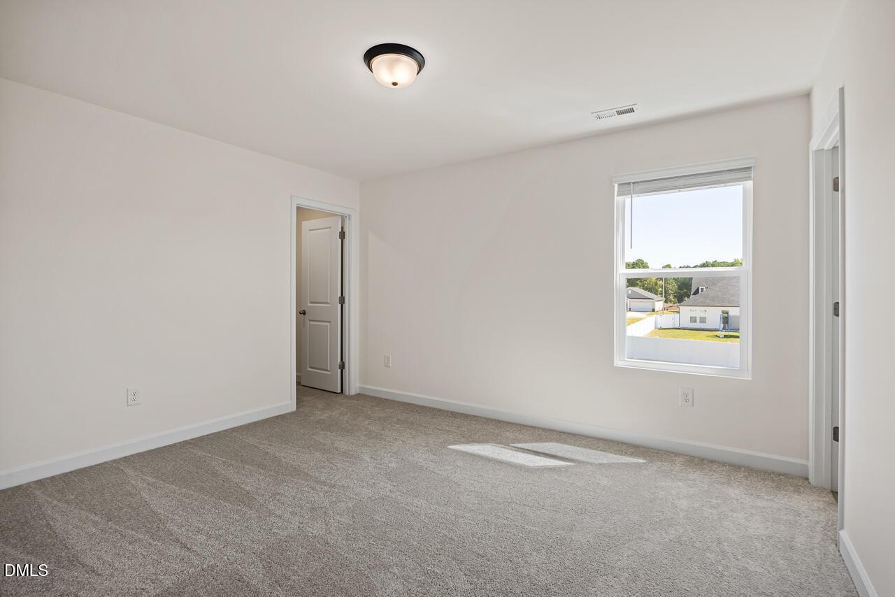 Bright empty bedroom with plush gray carpet, white walls, and sunny window in Davidson Homes' Hickory II B, Lillington, NC