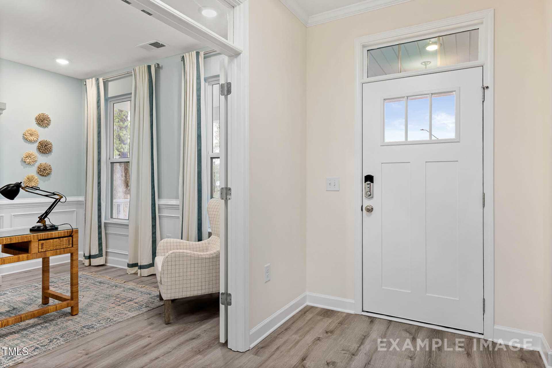 Cozy home office with wooden desk, tufted armchair, sheer curtains, and entry door in Davidson Homes The Magnolia B, Lillington NC