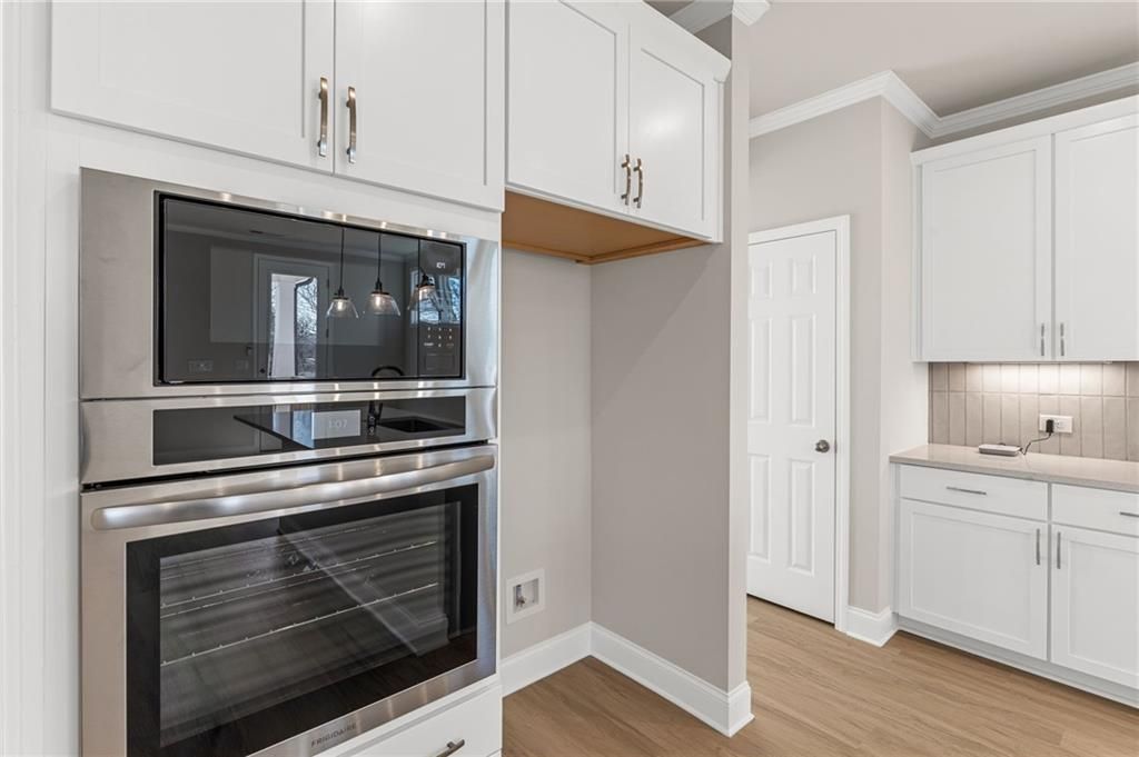 Modern white kitchen with stainless steel double oven, pendant lights, and open shelving in Davidson Homes The Willow B plan, Hoschton, GA