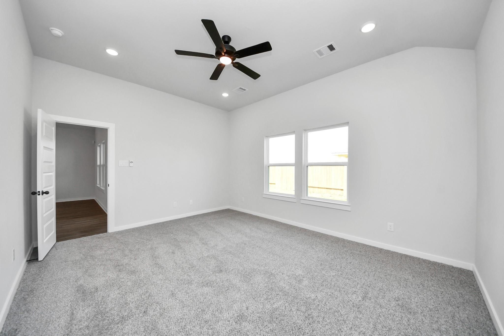Spacious bedroom with plush carpeting and ceiling fan in The Riviera C floor plan at River Ranch Meadows, Dayton, Texas.