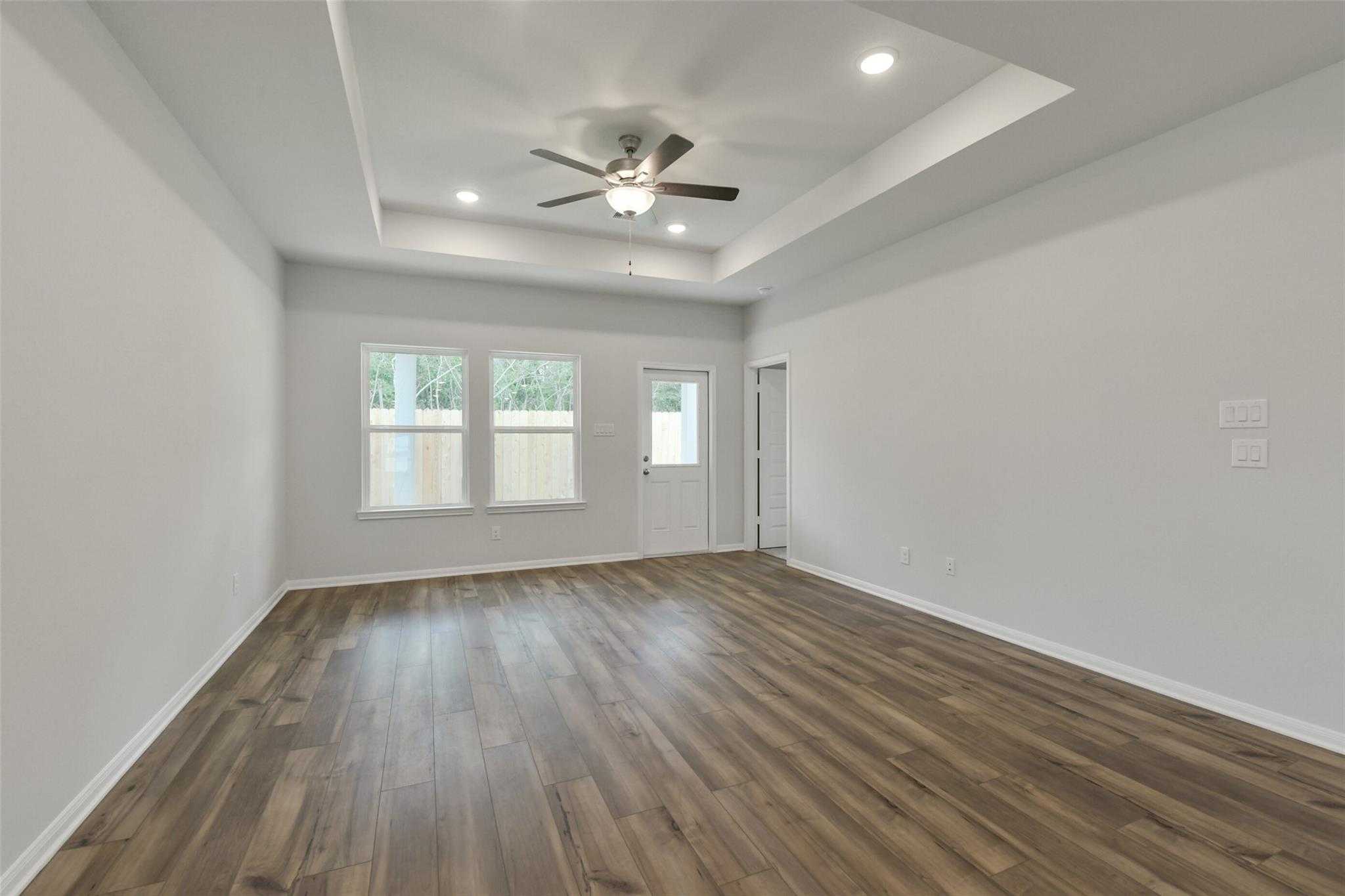 Spacious living room with hardwood floors, ceiling fan, recessed lights, and large windows in Davidson Homes The Frio G, Conroe, Texas